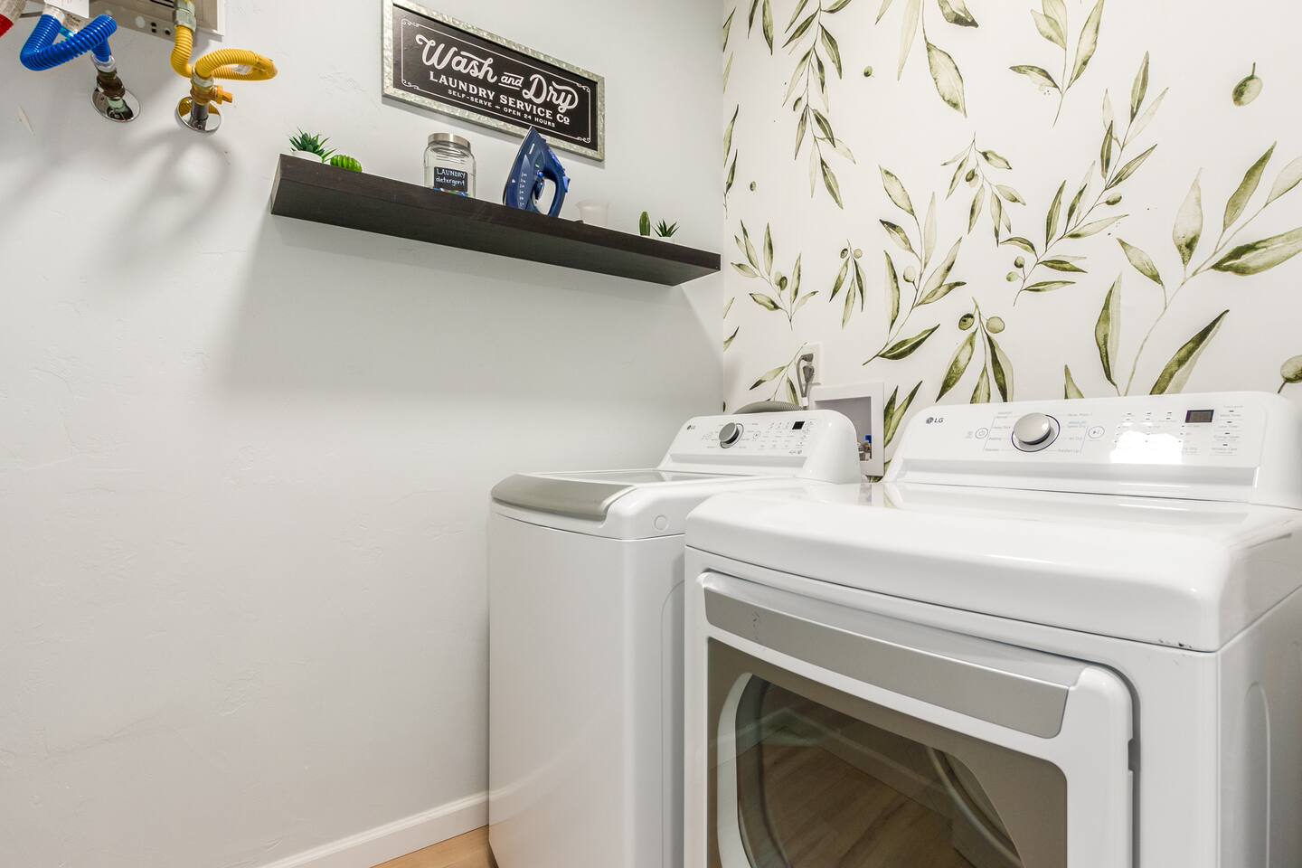 Enjoy the convenience of a fully equipped laundry room featuring a washer and dryer, iron and ironing board, and laundry hamper—all set against a charming wallpaper accent wall for a touch of style.