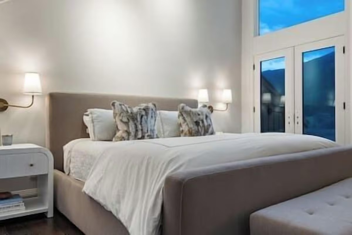 Bright, serene bedroom with plush bed, high ceilings, and elegant lighting