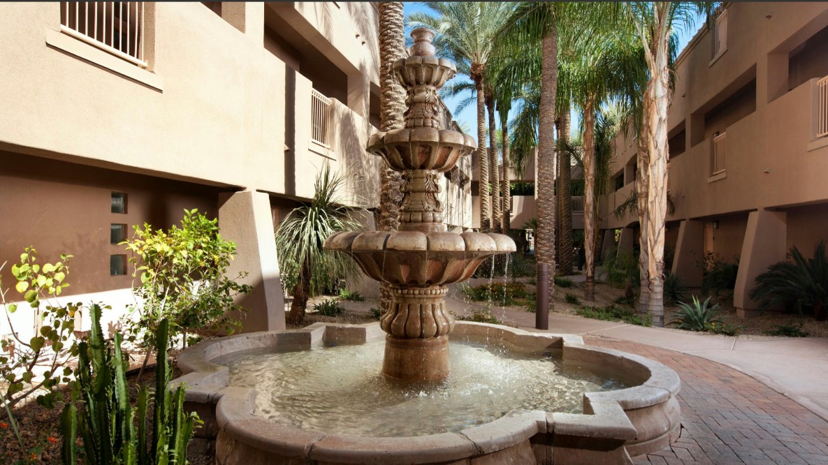 Resort-style courtyard with palm trees and an elegant stone fountain