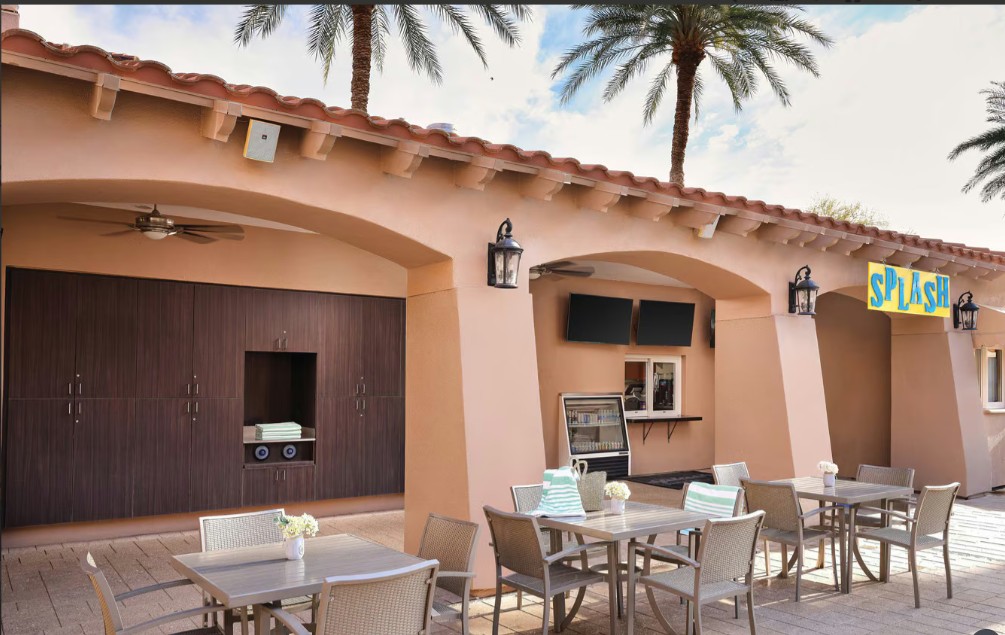 Covered resort-style patio with TVs, dining tables, and palm tree views