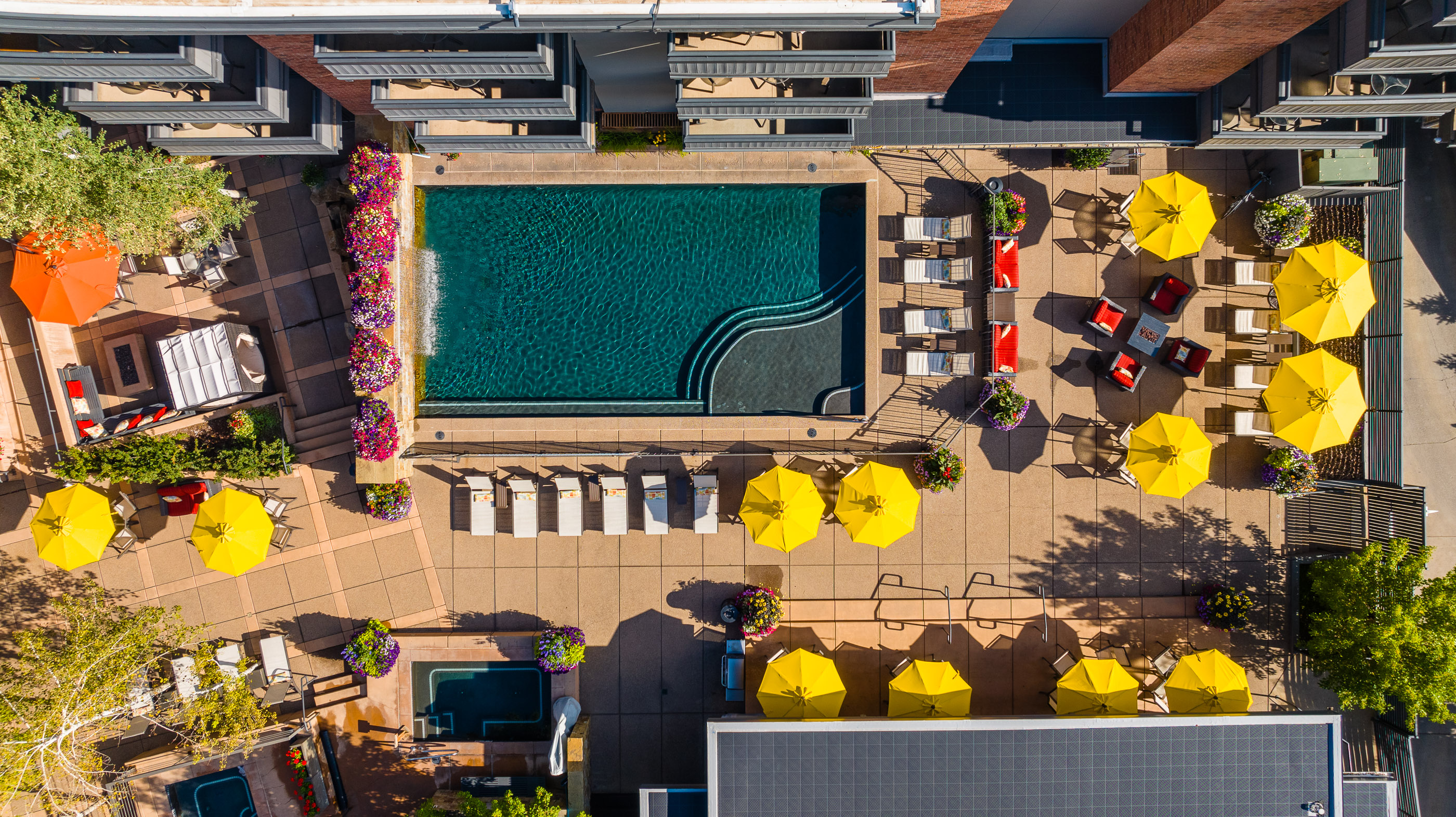 Resort-style pool deck with loungers, hot tub, and sunny umbrella seating