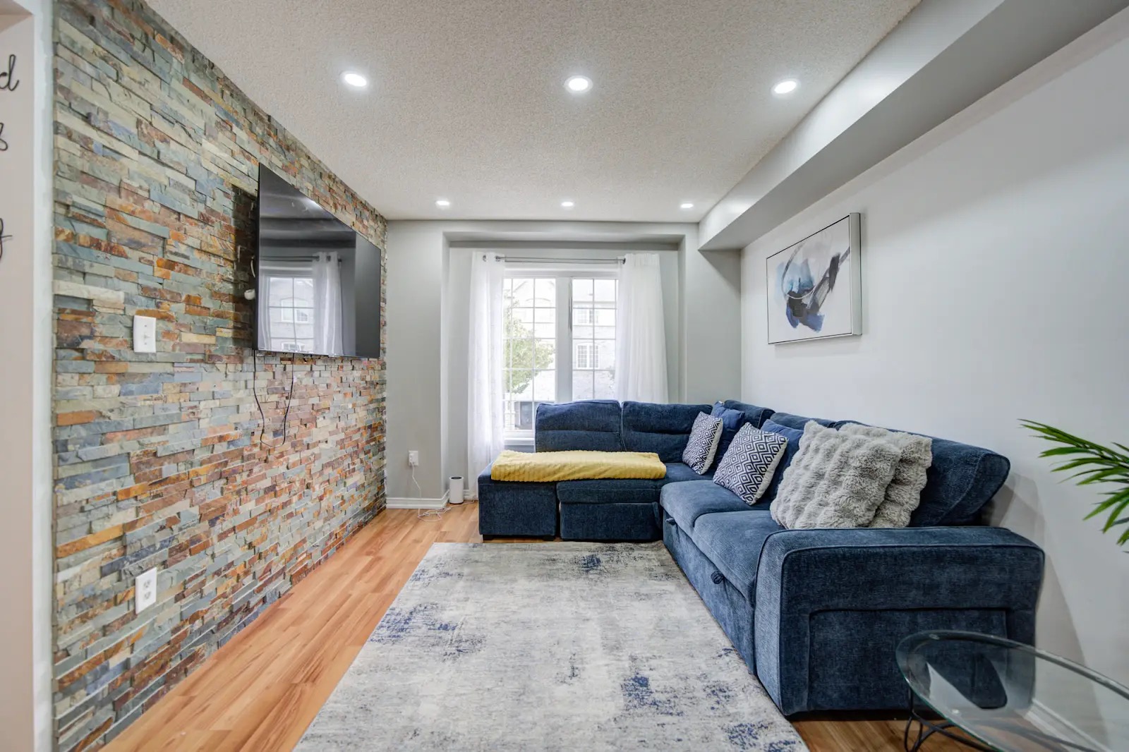 Cozy living room with blue sectional, stone accent wall, and smart TV