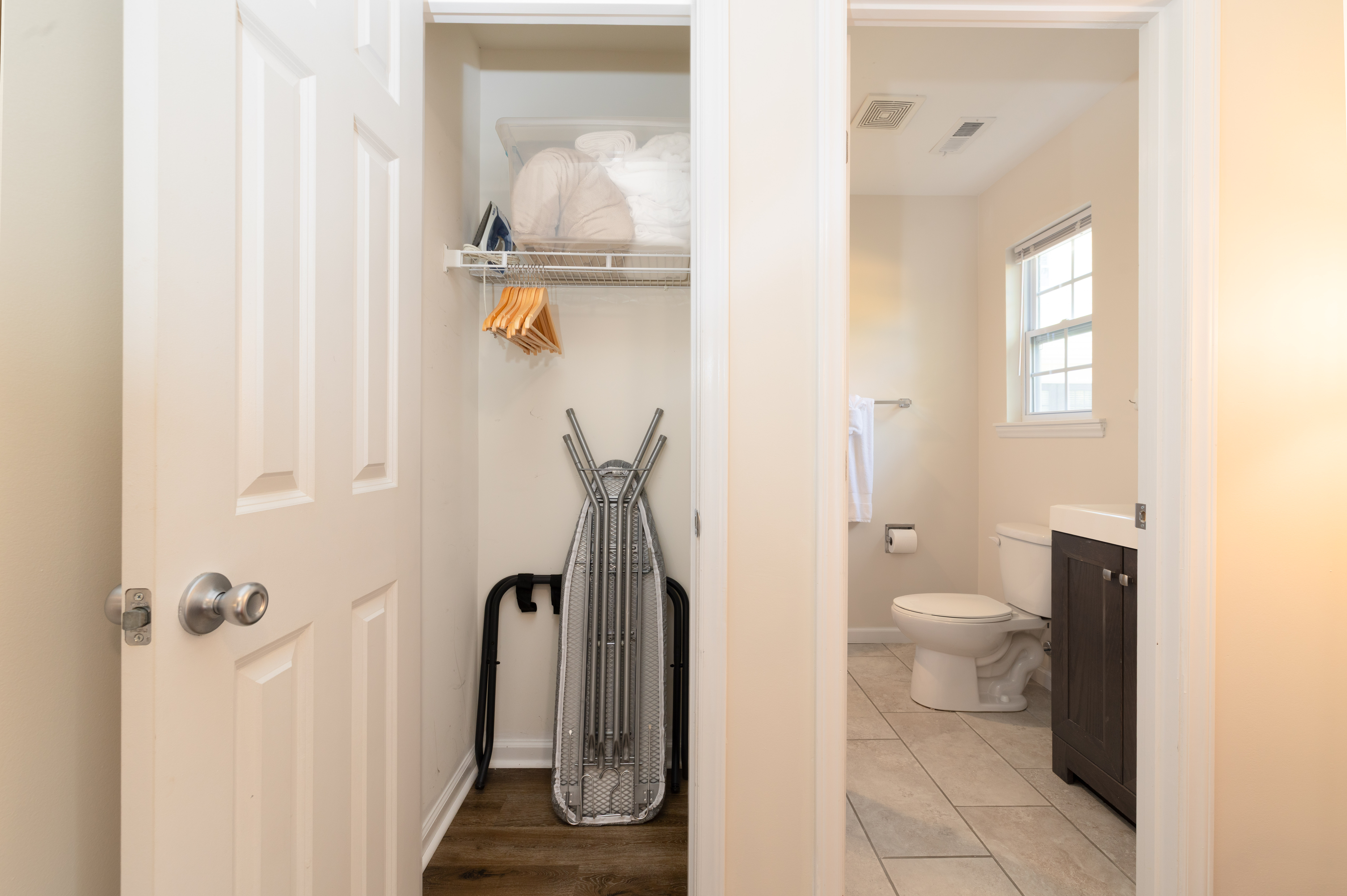 Closet with extra pillows, hangers and an ironing board, next to the primary en suite