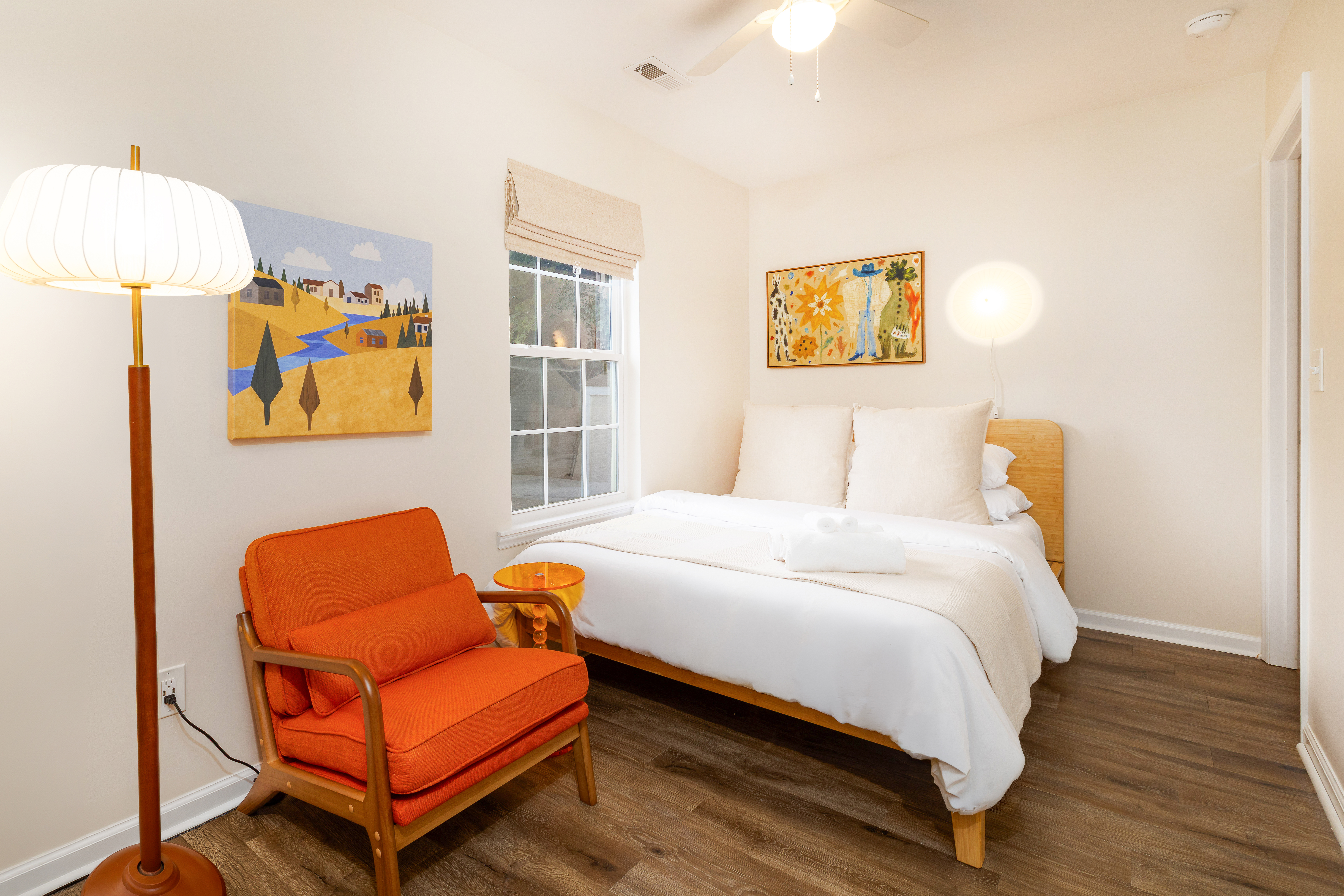 Primary bedroom with a queen bed, reading chair and blackout roman shade