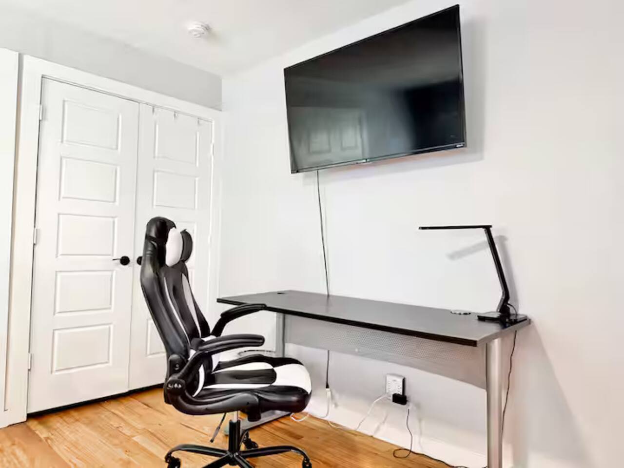 Stay productive in this sleek, dedicated workspace! Featuring a comfortable ergonomic gaming chair, a spacious desk with a modern LED lamp, and a large wall-mounted monitor, it's the perfect setup for remote work or gaming.