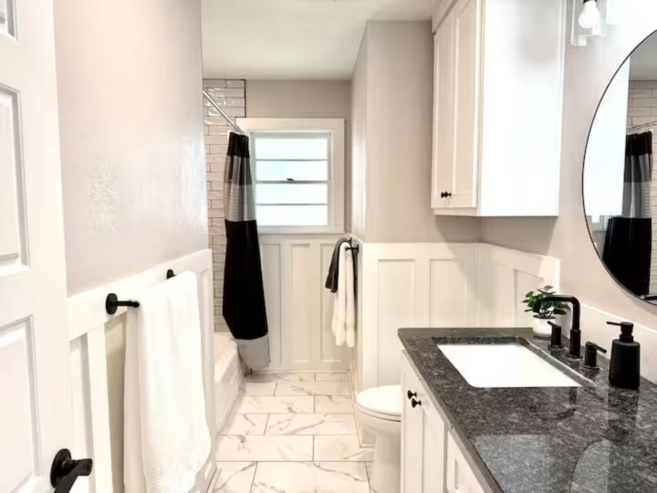 Refresh in this spa-like bathroom featuring elegant marble-style flooring and chic wainscoting. Enjoy a granite vanity, modern matte black fixtures, and a clean, bright atmosphere designed for your total relaxation.