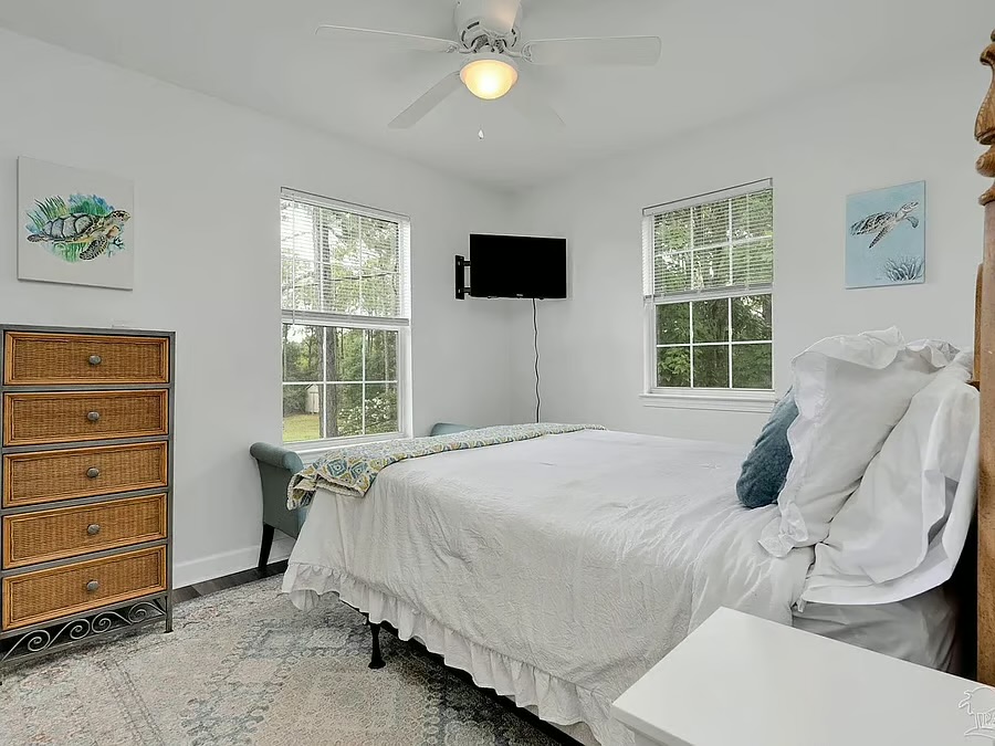 Bright coastal bedroom with natural light, TV, and crisp white bedding