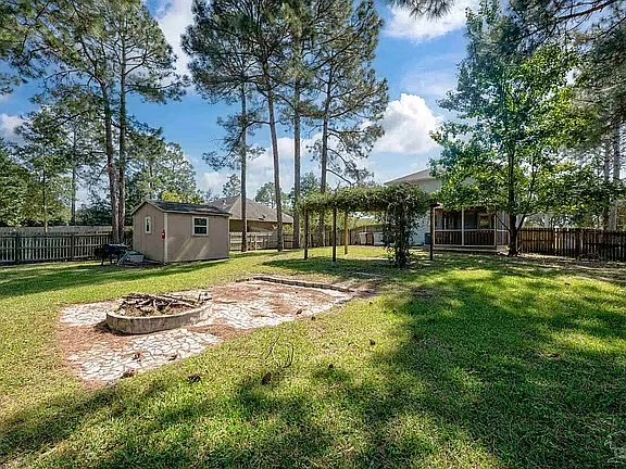 Spacious fenced backyard with fire pit, pergola, and towering trees
