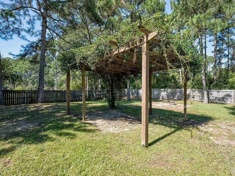 Private fenced backyard with vine-covered pergola and serene wooded setting