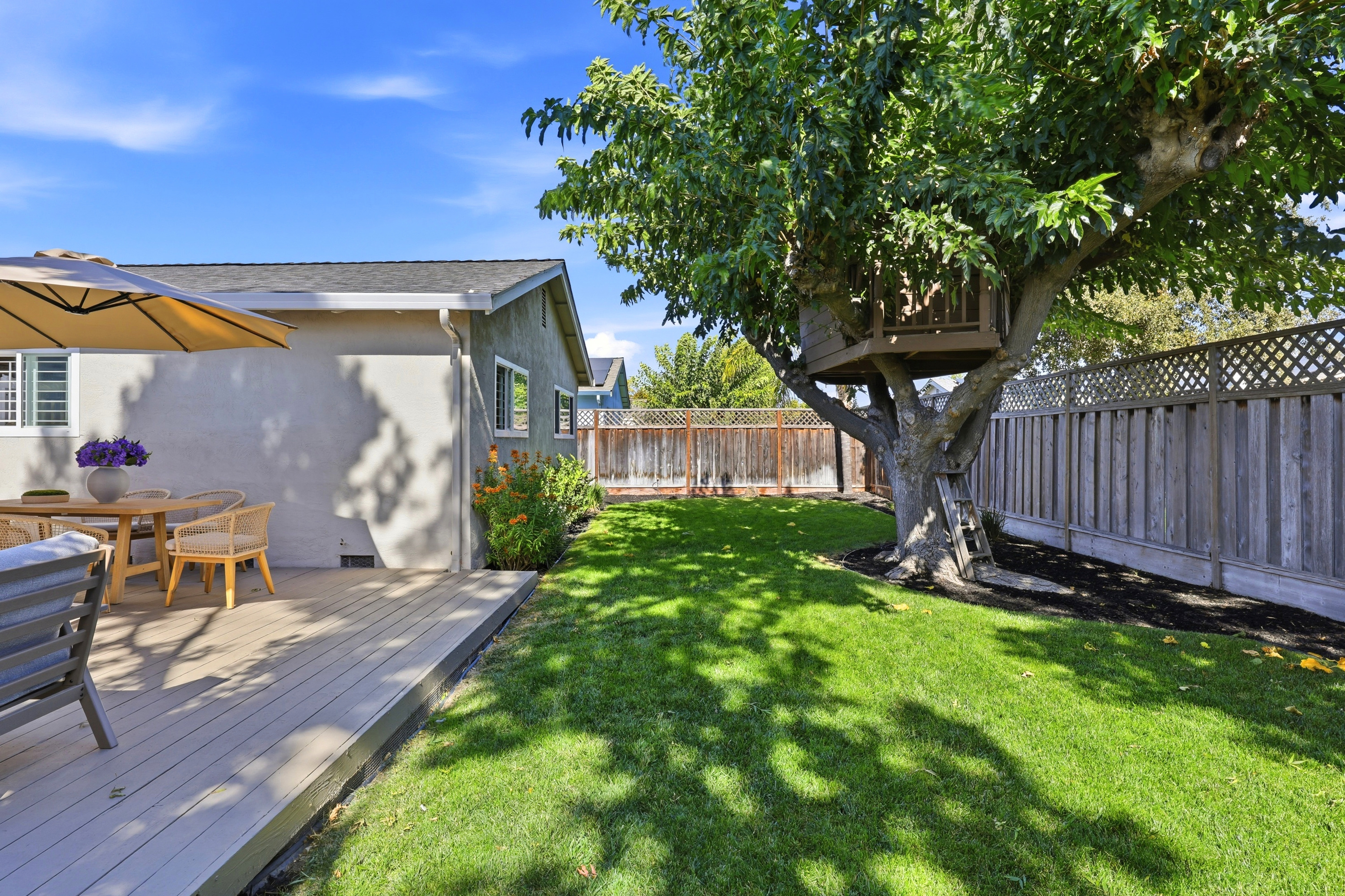 Private backyard with sunny deck, lush lawn, and charming treehouse