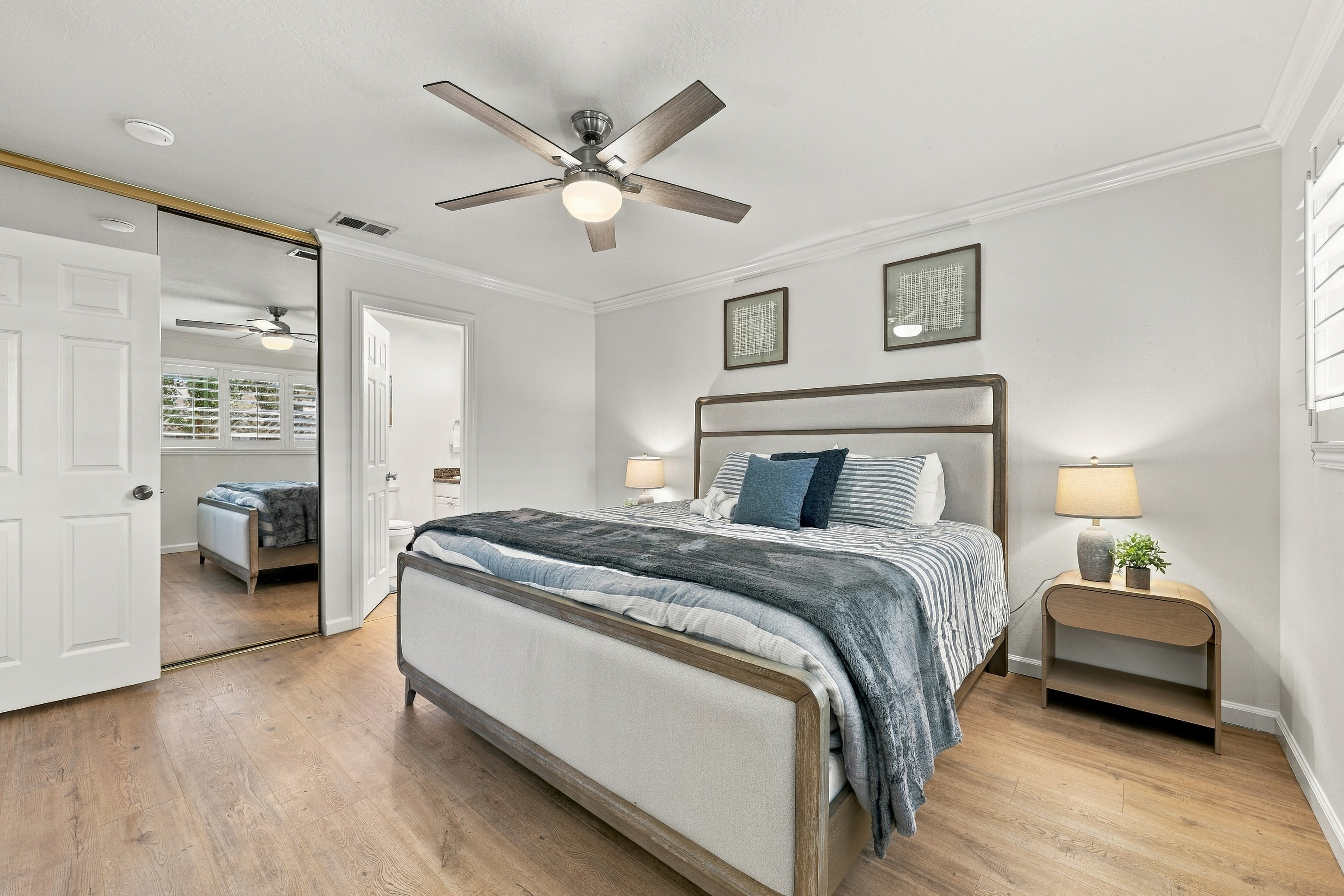 Bright, stylish Primary bedroom with king bed, bathroom, ceiling fan, and mirrored closet