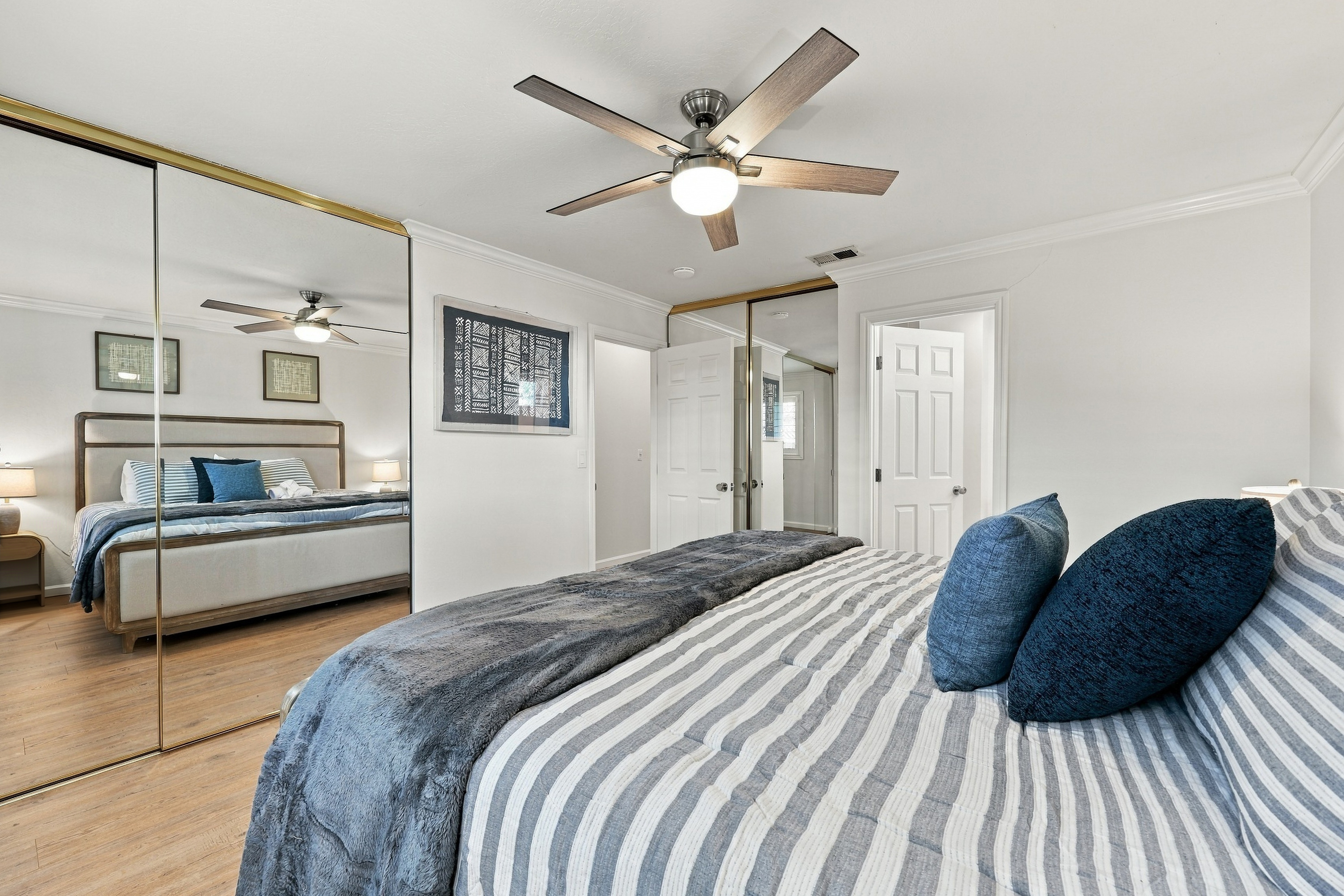 Bright bedroom with mirrored closets, cozy bedding, and ceiling fan