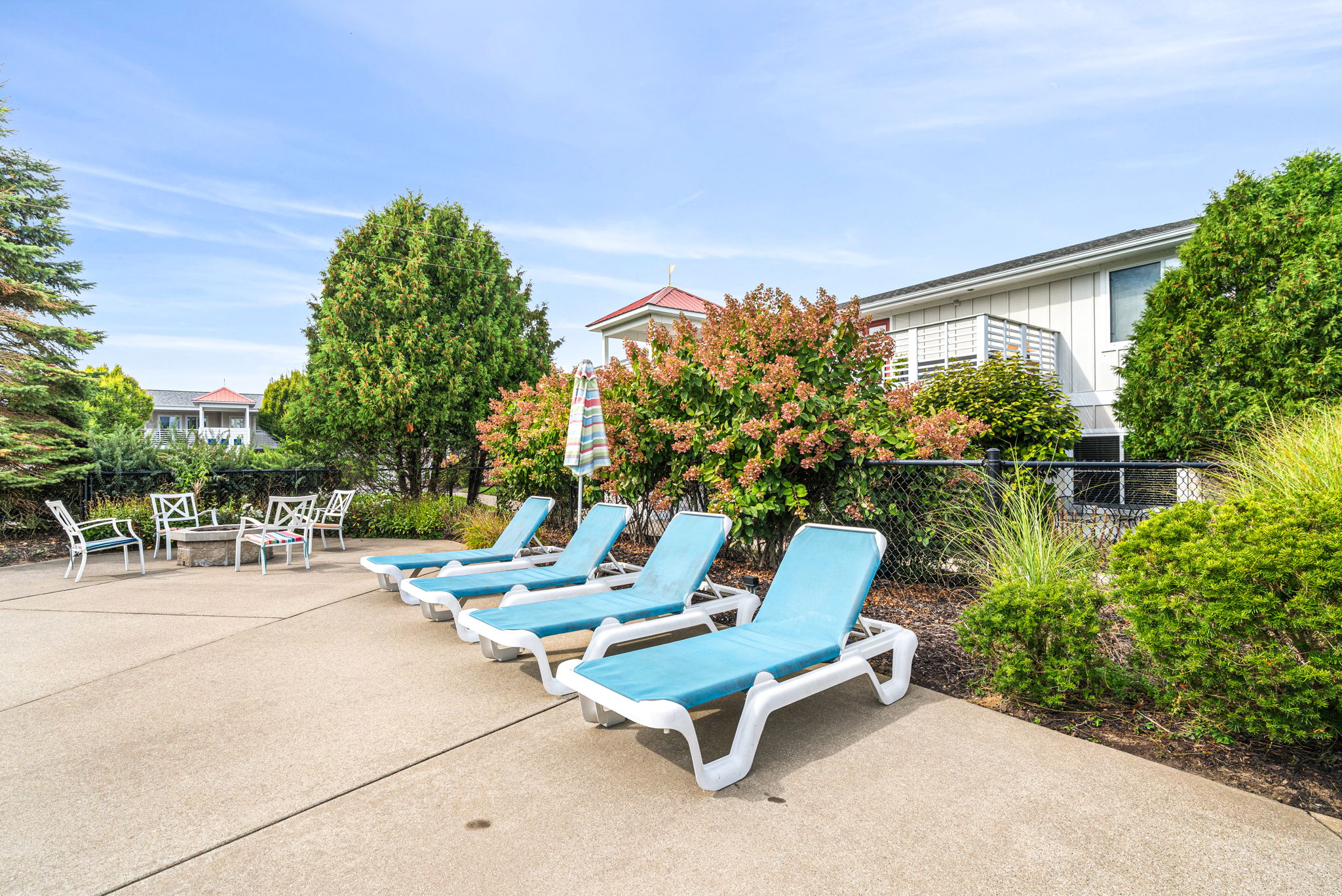 Sunny poolside lounge area with fire pit seating and landscaped privacy
