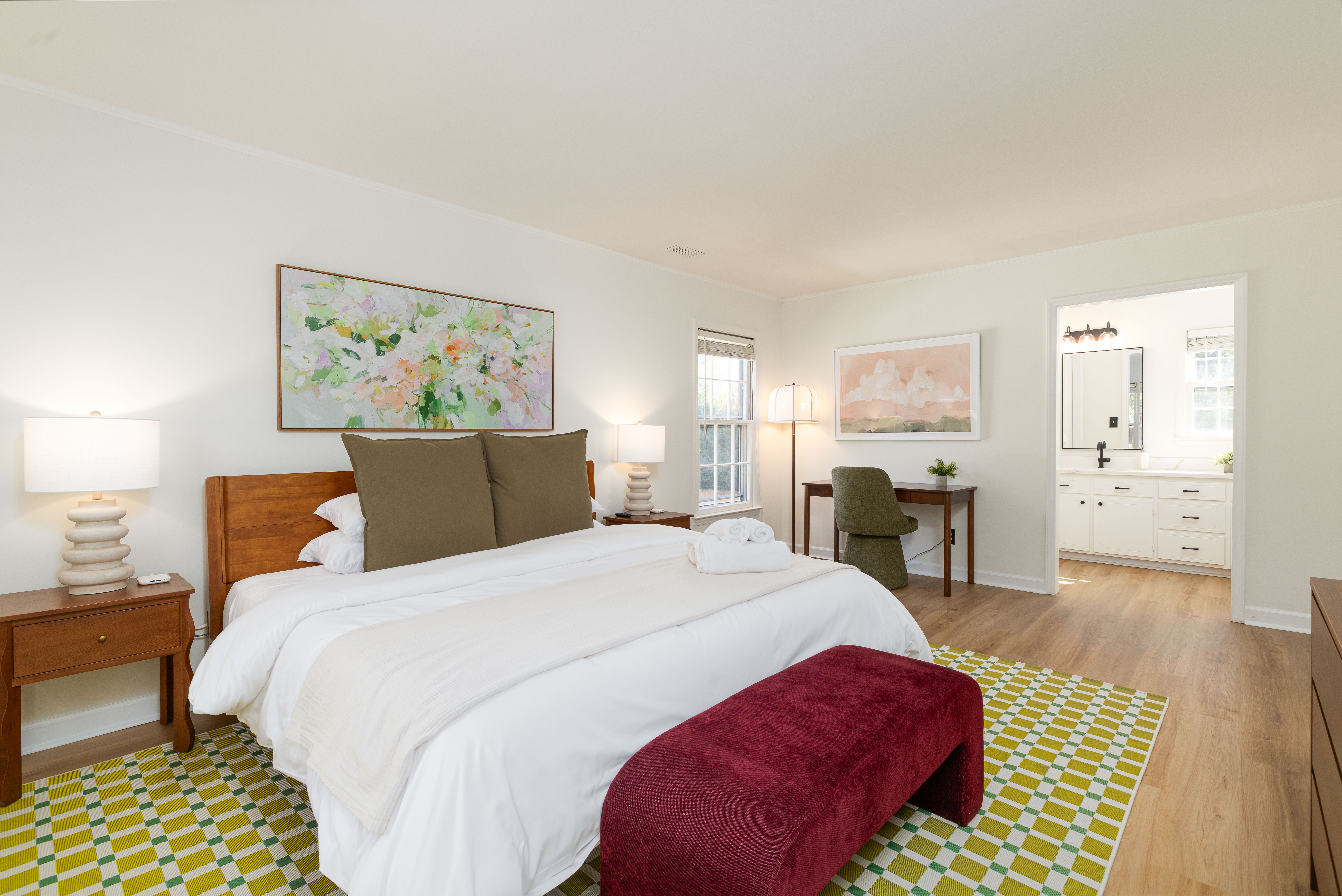 Primary suite: king bed with a bench at the foot, a desk, and the en suite beyond