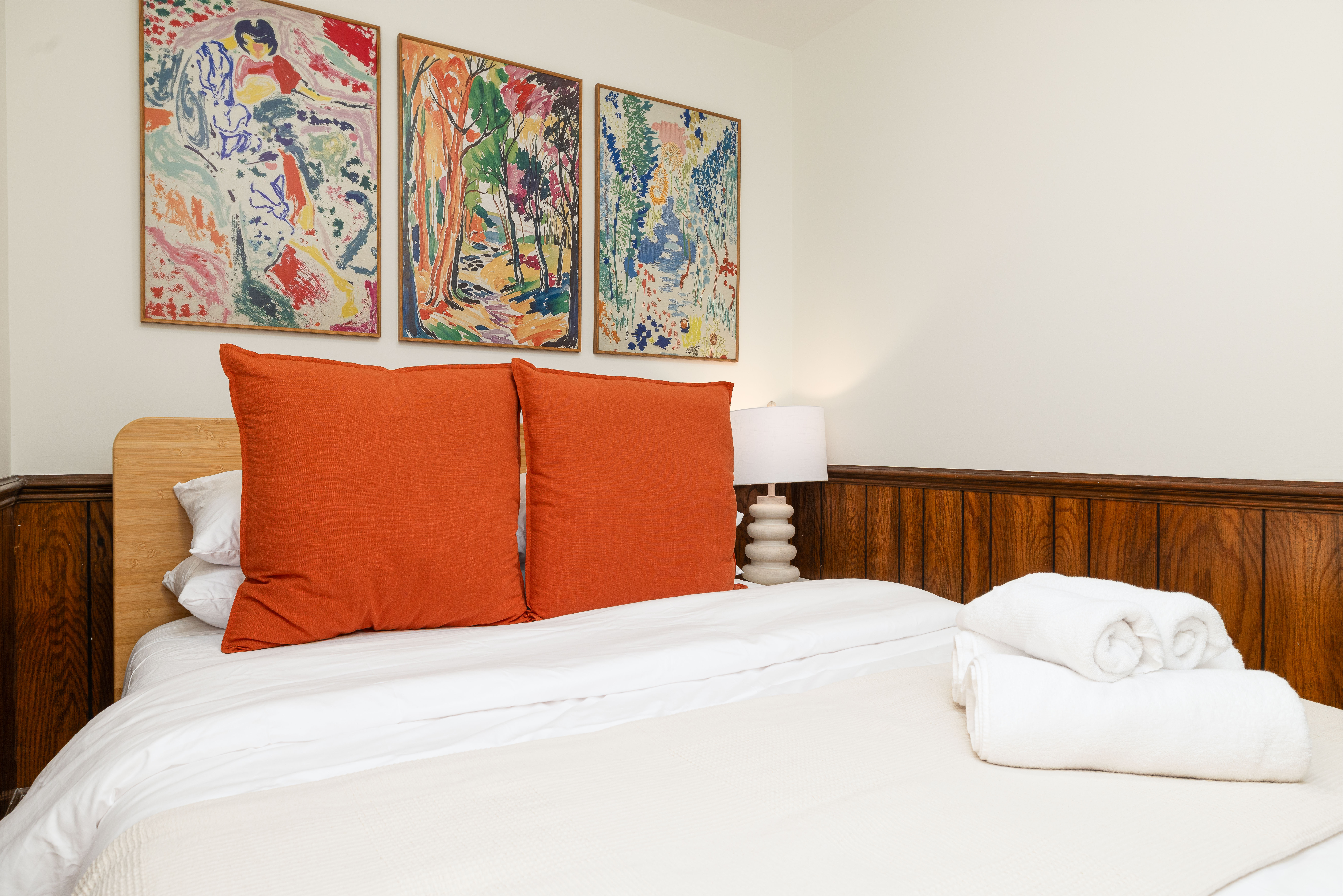 Bedroom 4 (downstairs): queen bed under three framed prints, with fresh towels