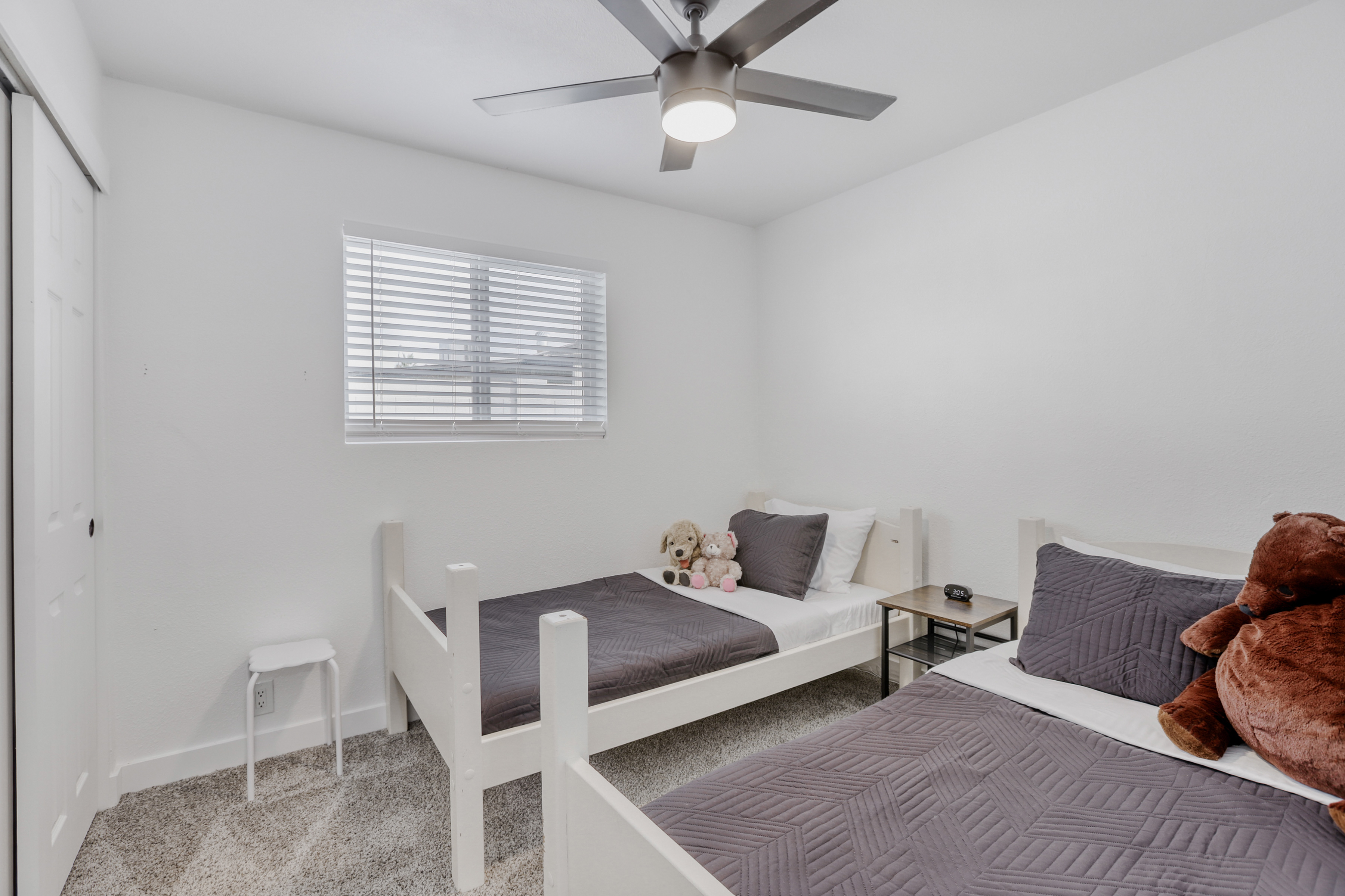 Bright twin bedroom with cozy bedding, ceiling fan, and kid-friendly charm