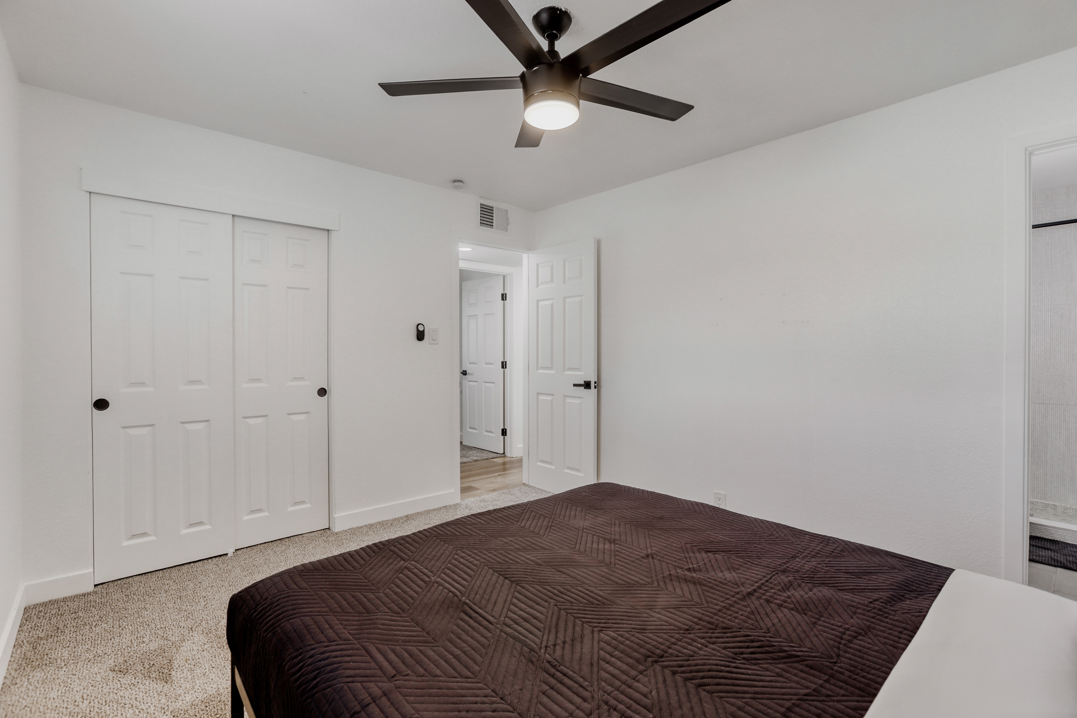 Bright, minimalist bedroom with soft carpet and modern ceiling fan