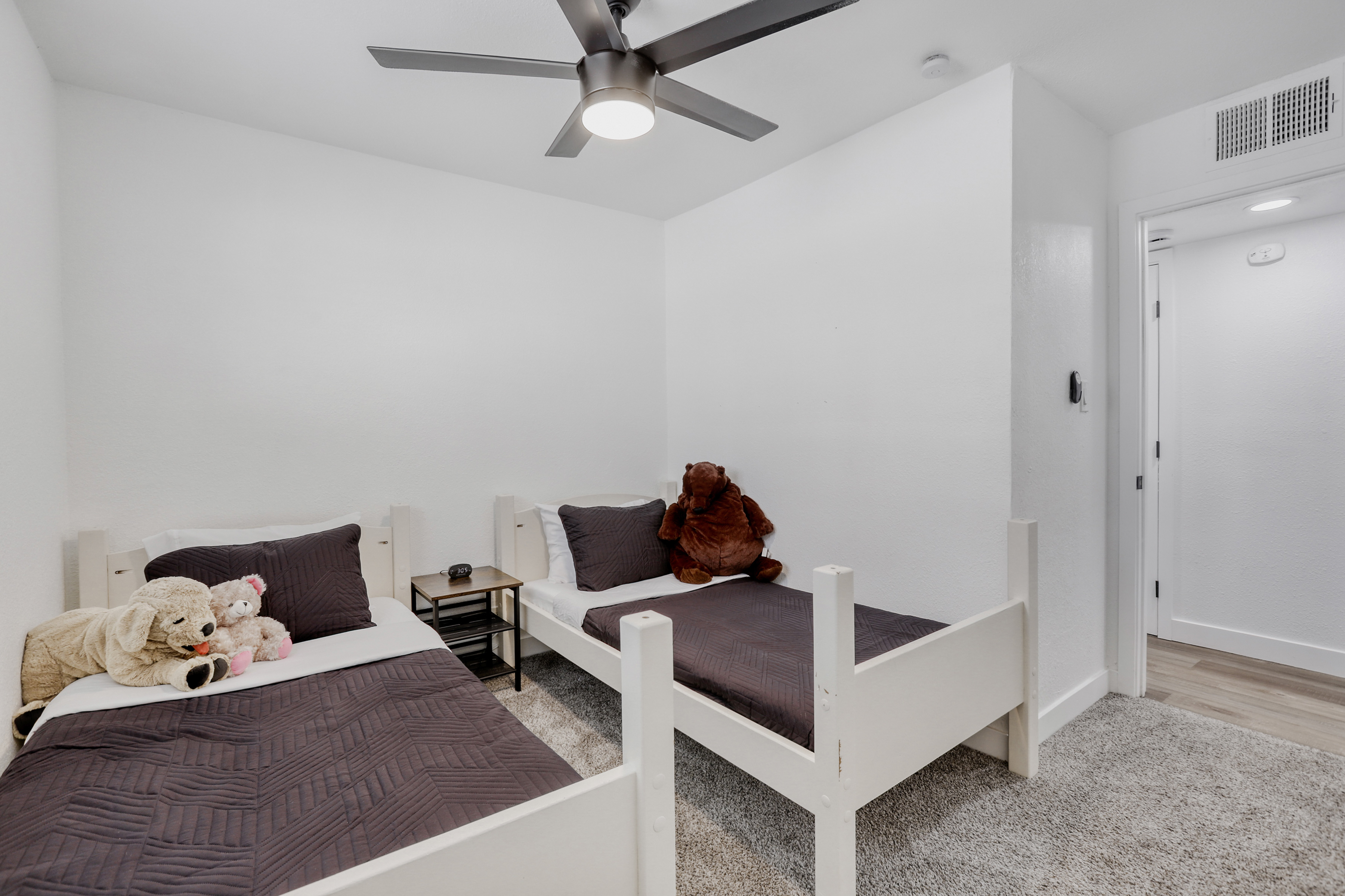 Bright twin bedroom with cozy beds, soft carpet, and modern ceiling fan