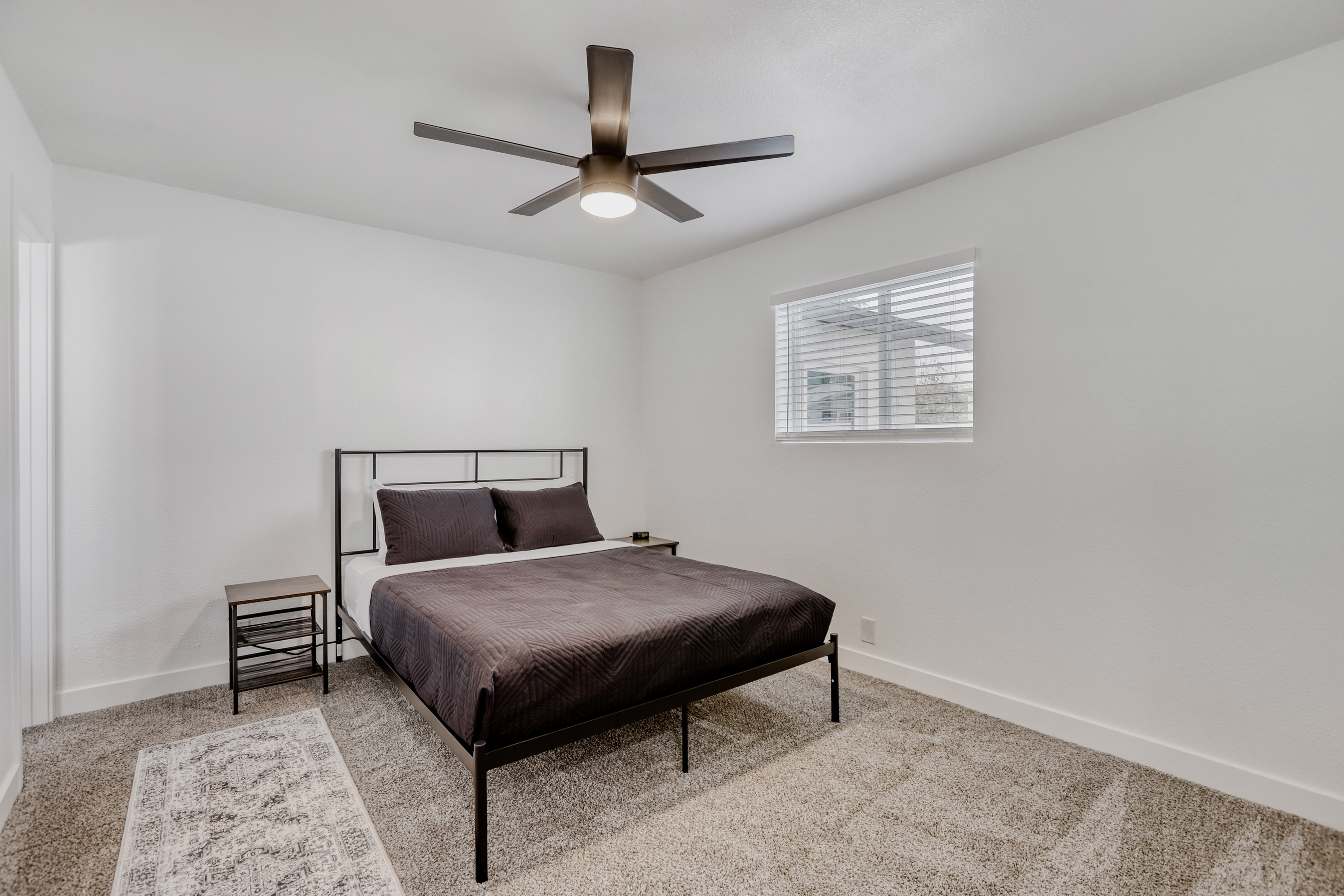 Bright minimalist bedroom with plush carpet and ceiling fan