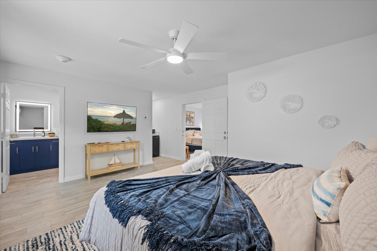 Bright coastal-style bedroom with TV, ceiling fan, and stylish vanity area