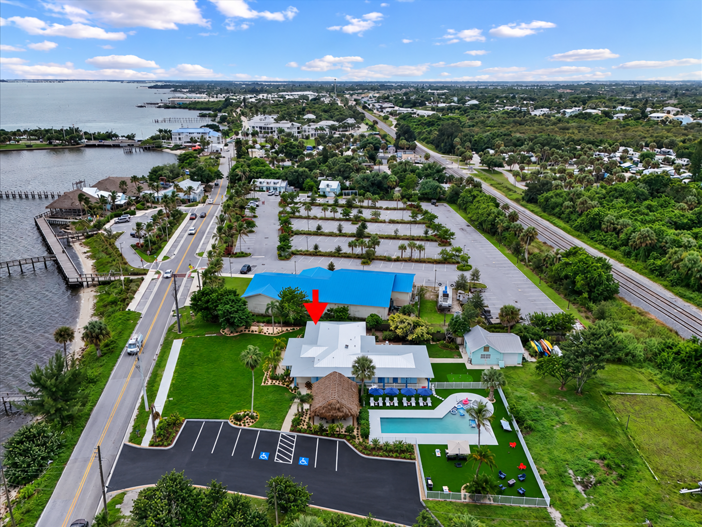 Aerial view of waterfront retreat with pool, tiki hut, and lush grounds