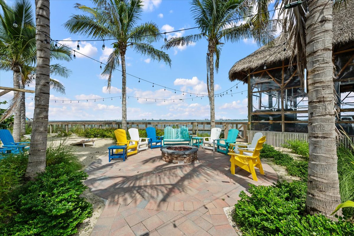 Tropical fire pit lounge with palm trees, string lights, and colorful seating