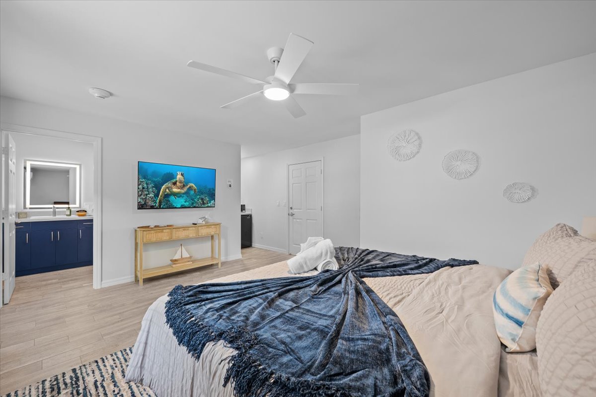 Bright coastal-style bedroom with TV, ceiling fan, and en suite vanity