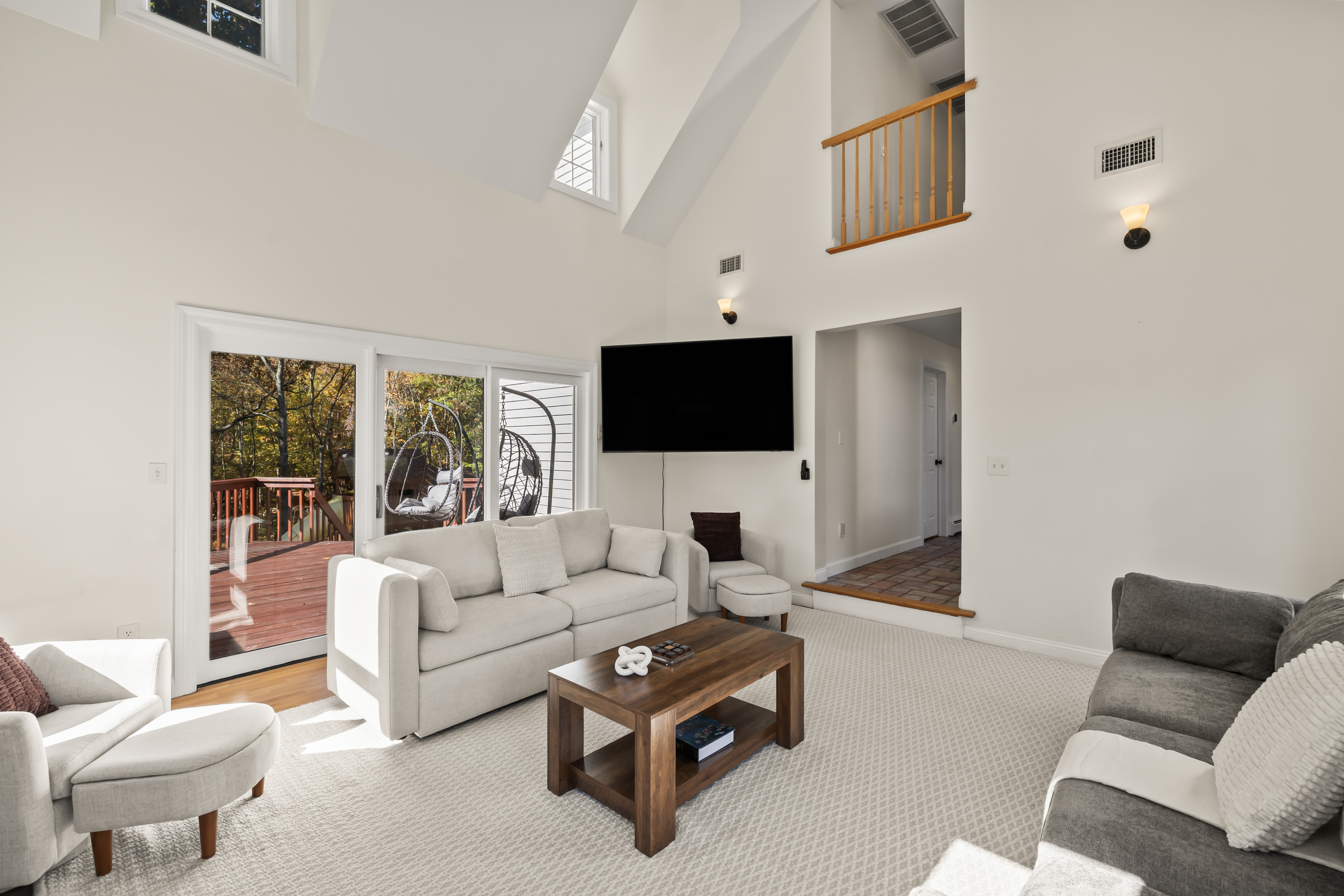 Vaulted living room with deck access, wooded views, and bright natural light