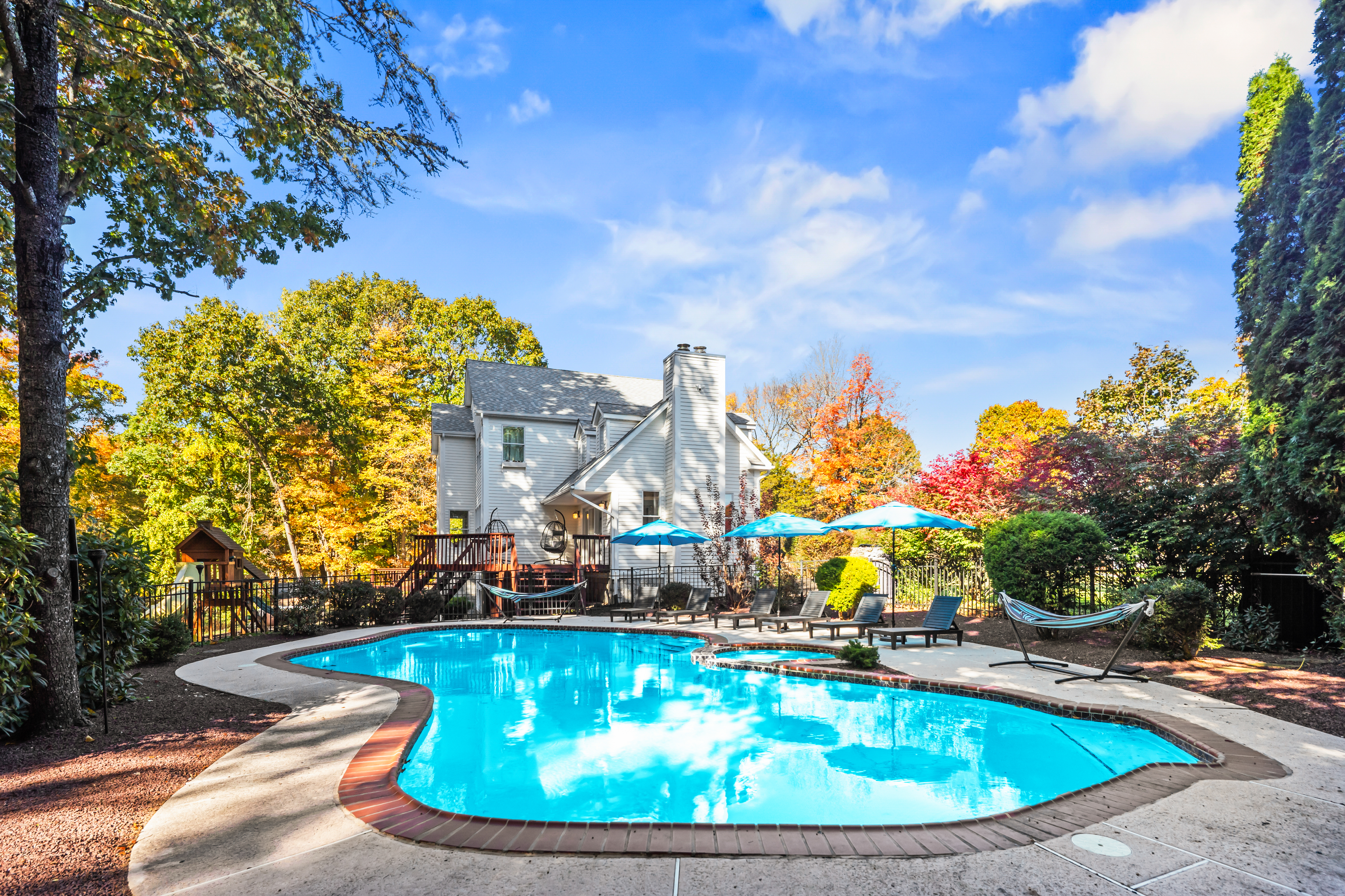 Private backyard pool oasis with lounge seating, deck, and colorful trees