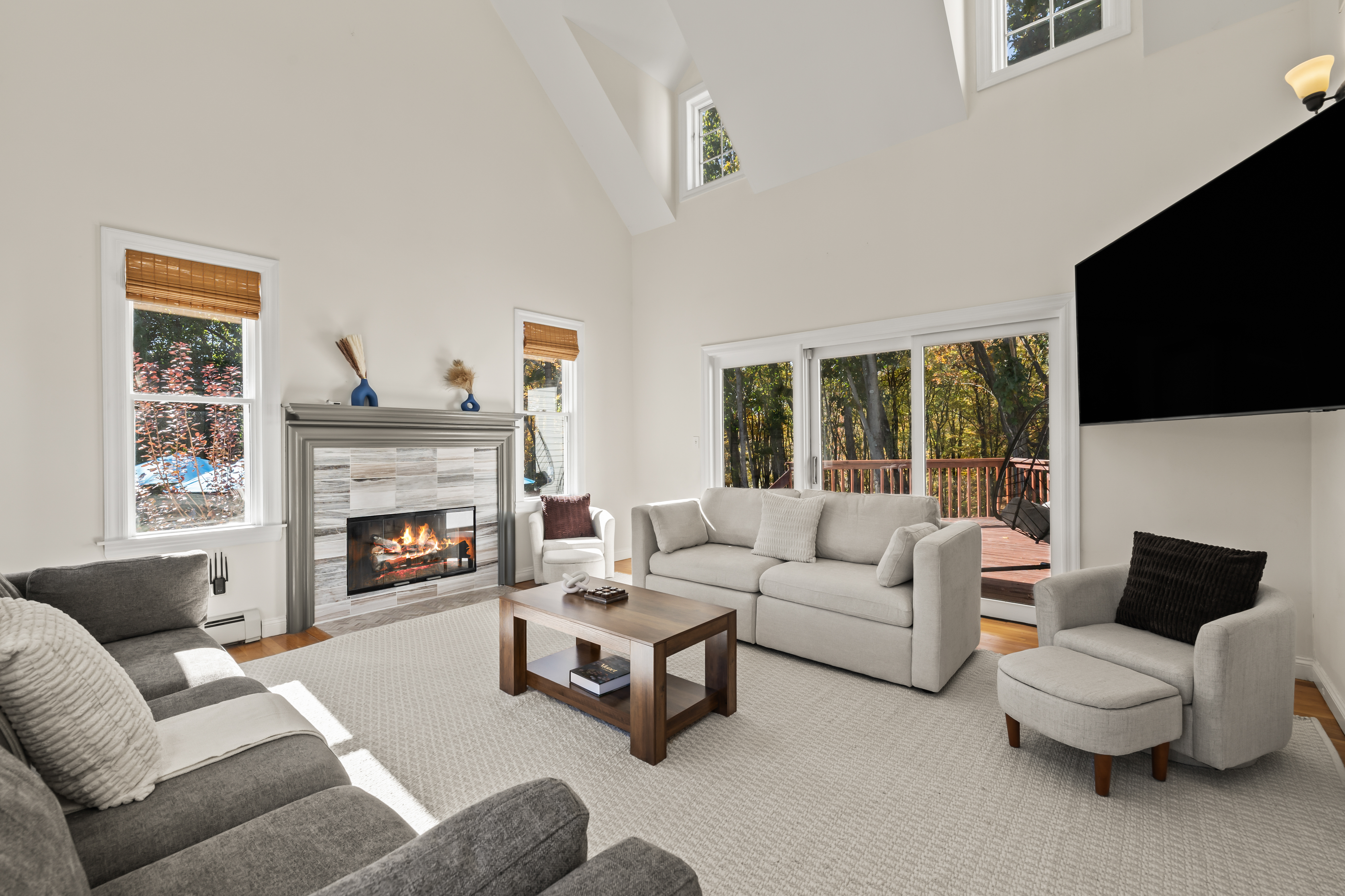 Bright vaulted living room with fireplace, TV, and deck views