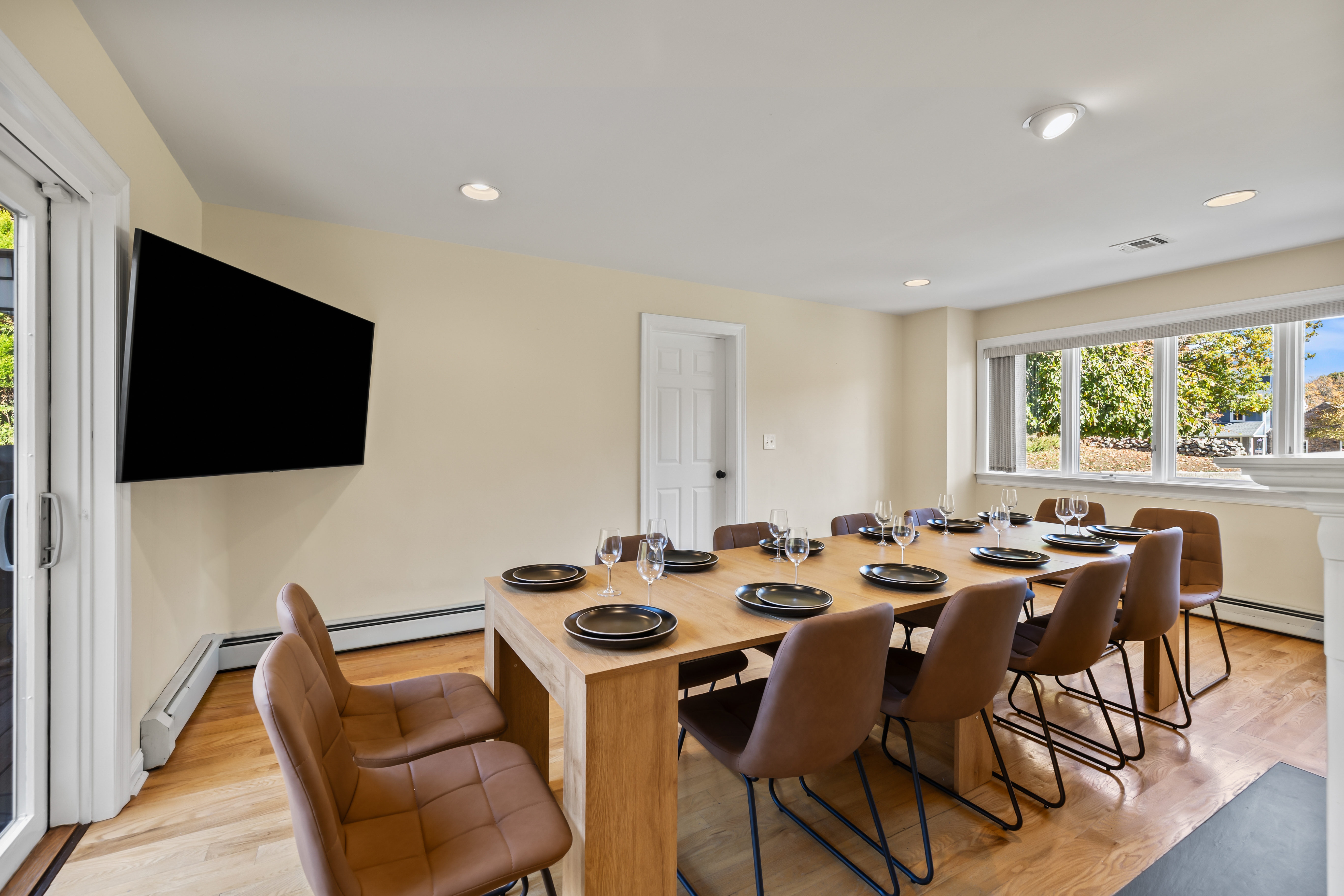 Bright dining room with seating for 10, big windows, and wall-mounted TV