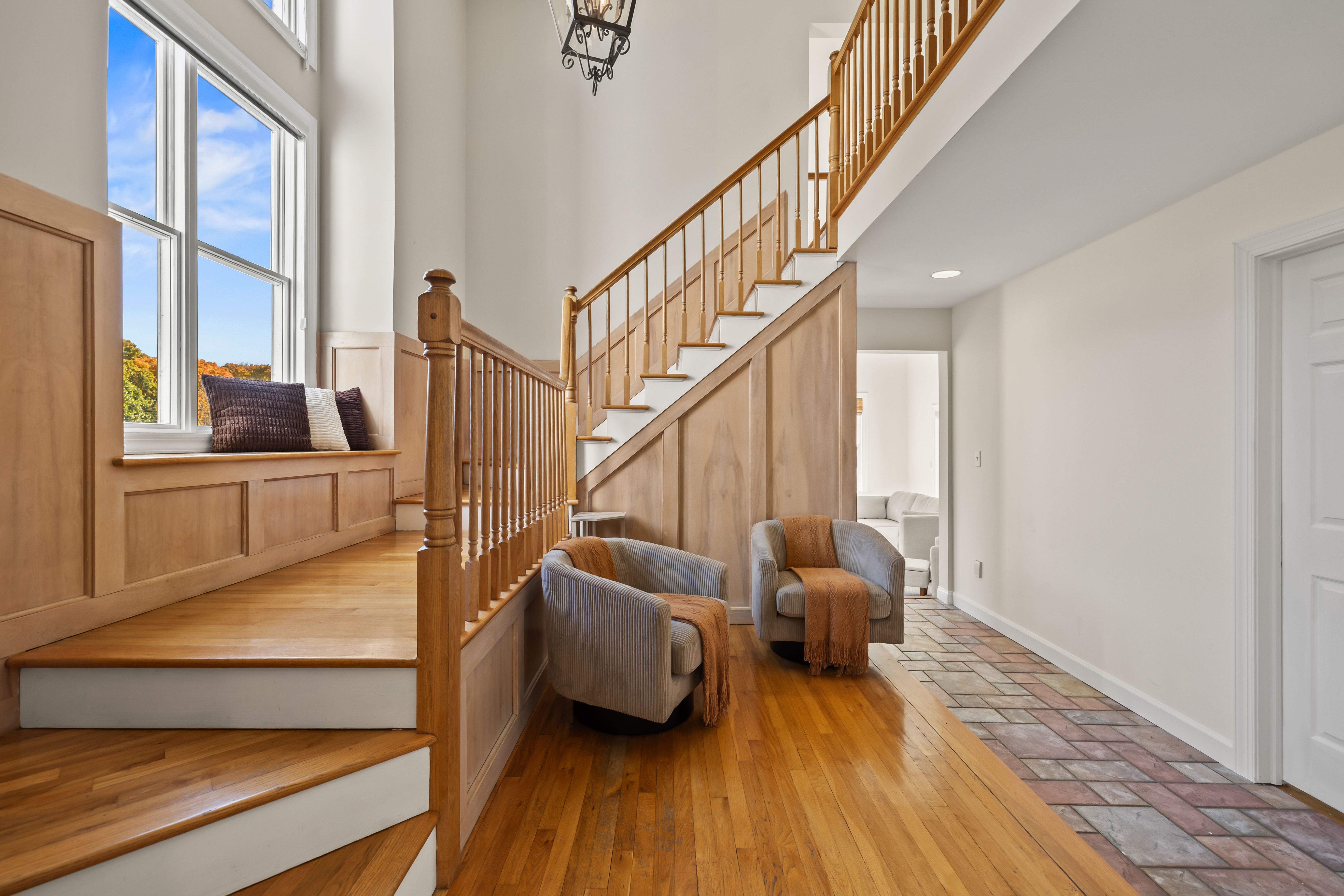 Grand sunlit entryway with hardwood floors, staircase, and cozy seating