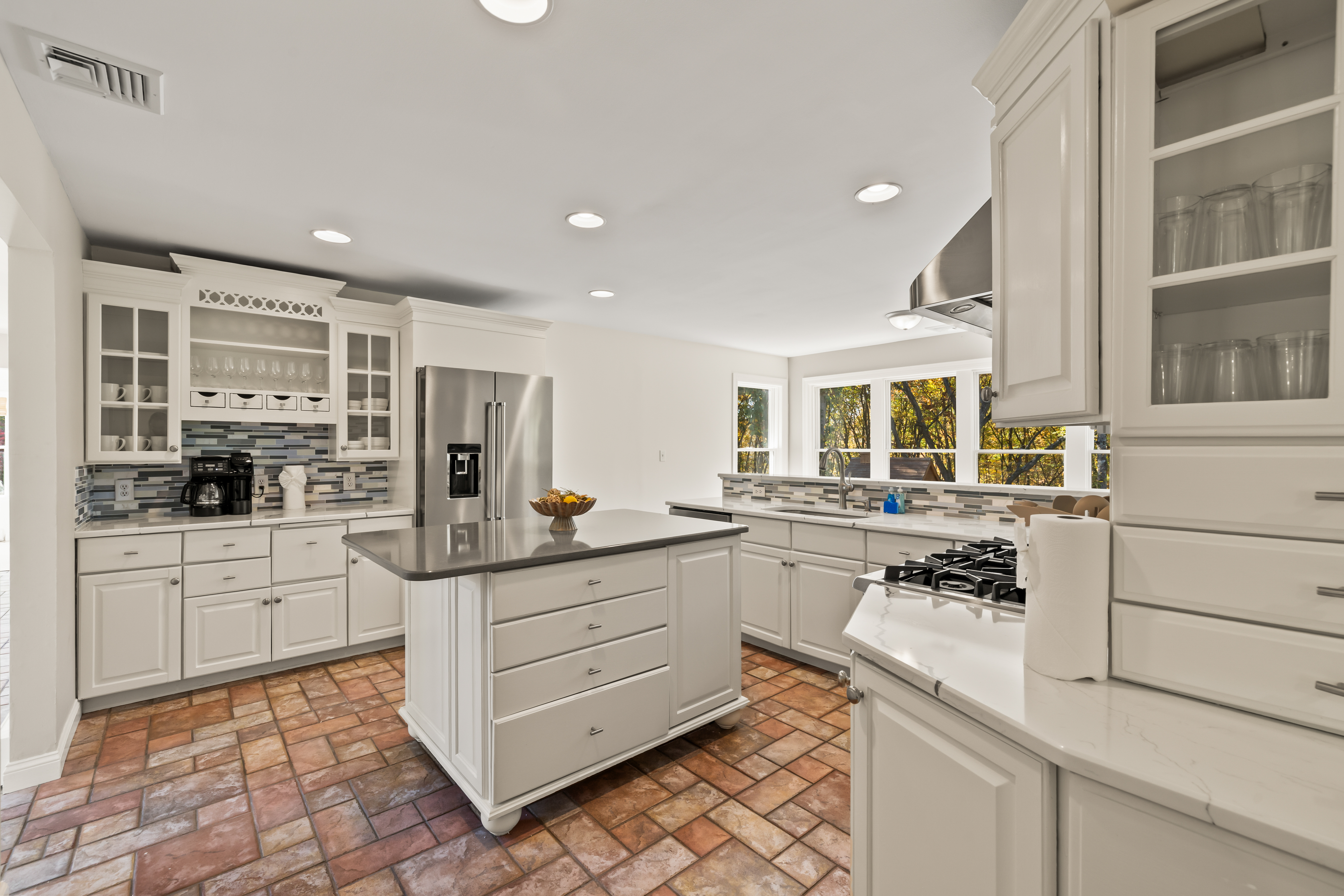 Bright chef’s kitchen with island, gas cooktop, and sunny treetop views