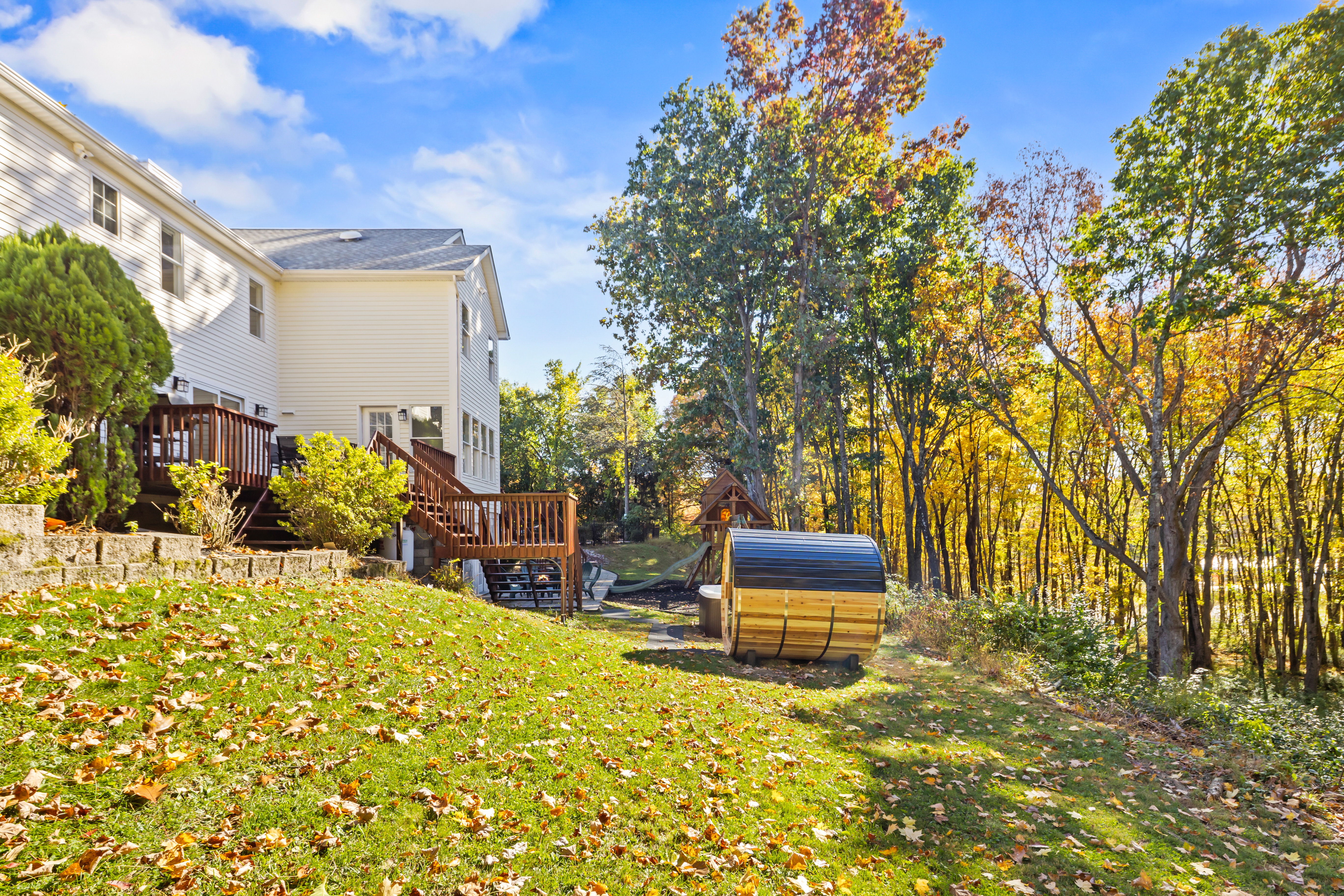Private backyard with deck, lawn, and sauna framed by beautiful fall trees