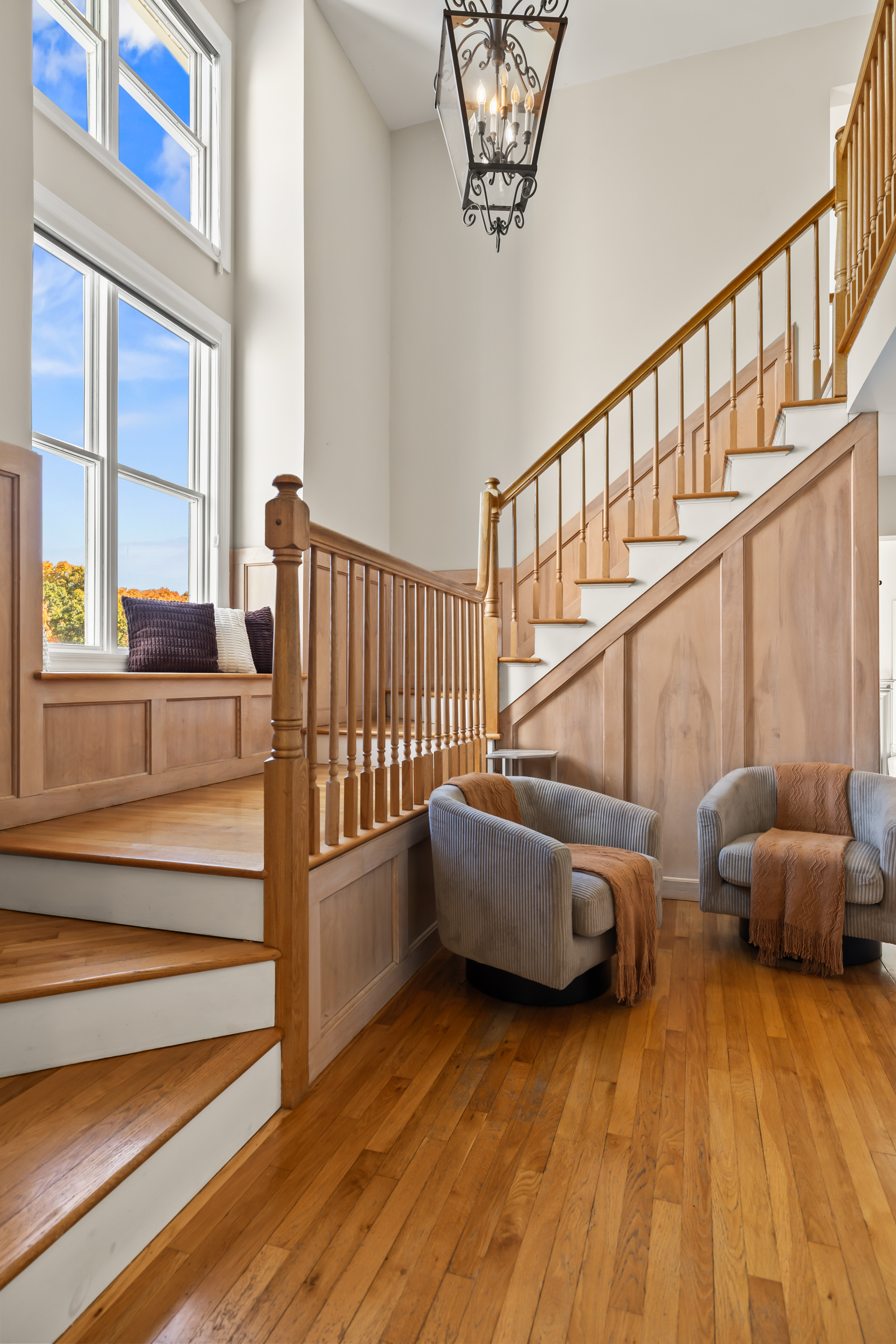 Sun-filled foyer with soaring ceilings, grand staircase, and cozy seating