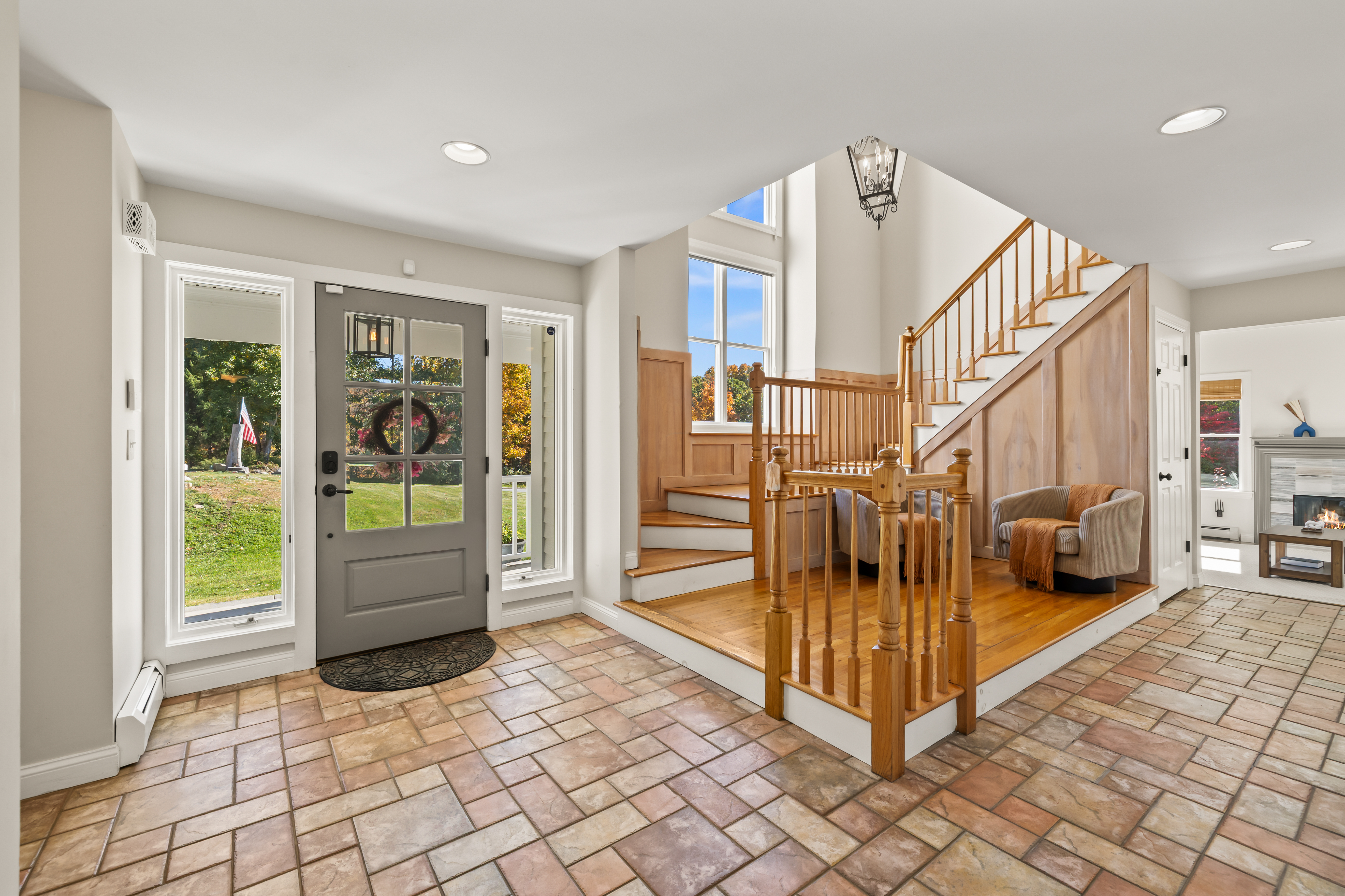 Bright entryway with soaring ceilings, tile floors, and warm wood staircase