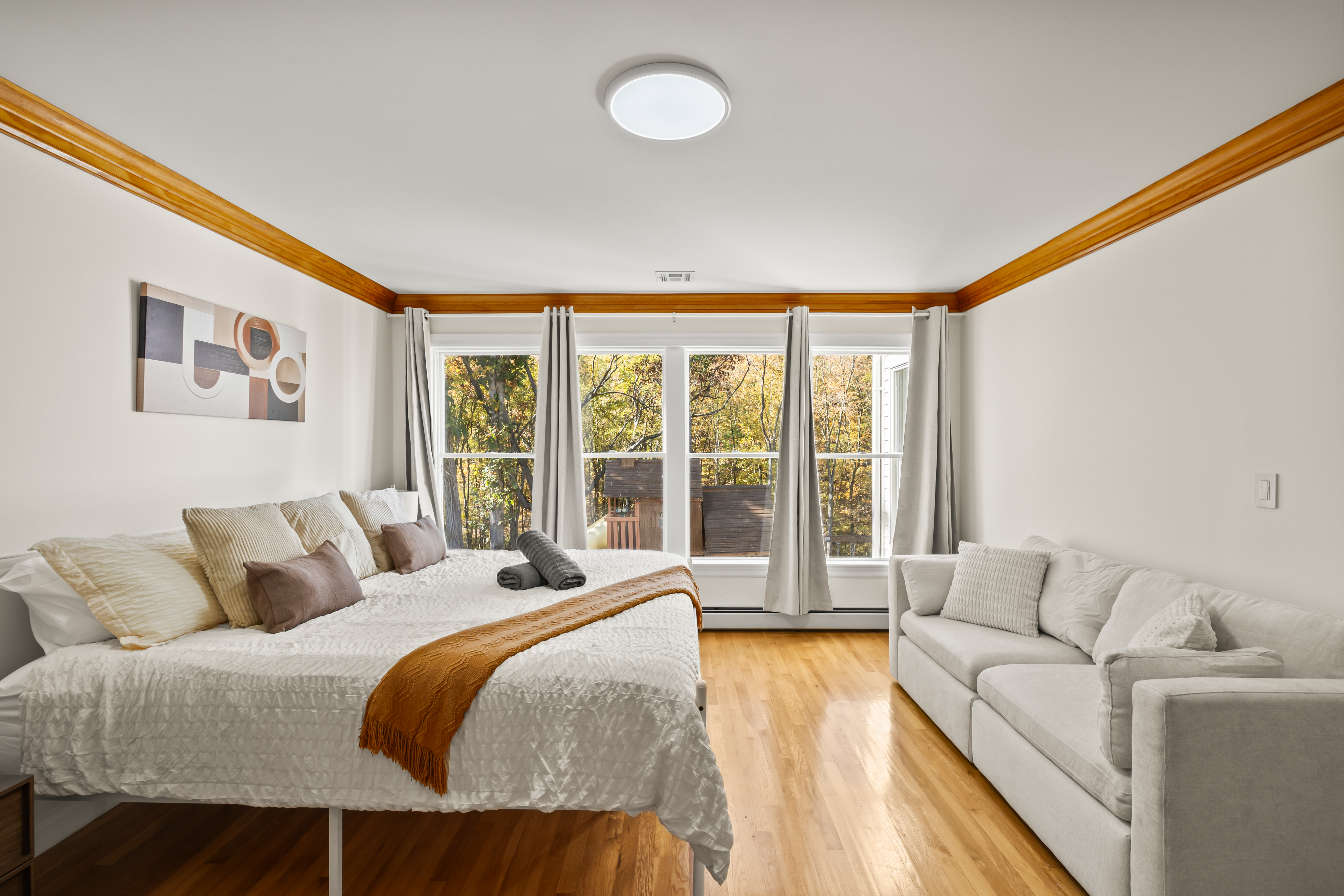 Bright bedroom with sofa, hardwood floors, and serene treetop views