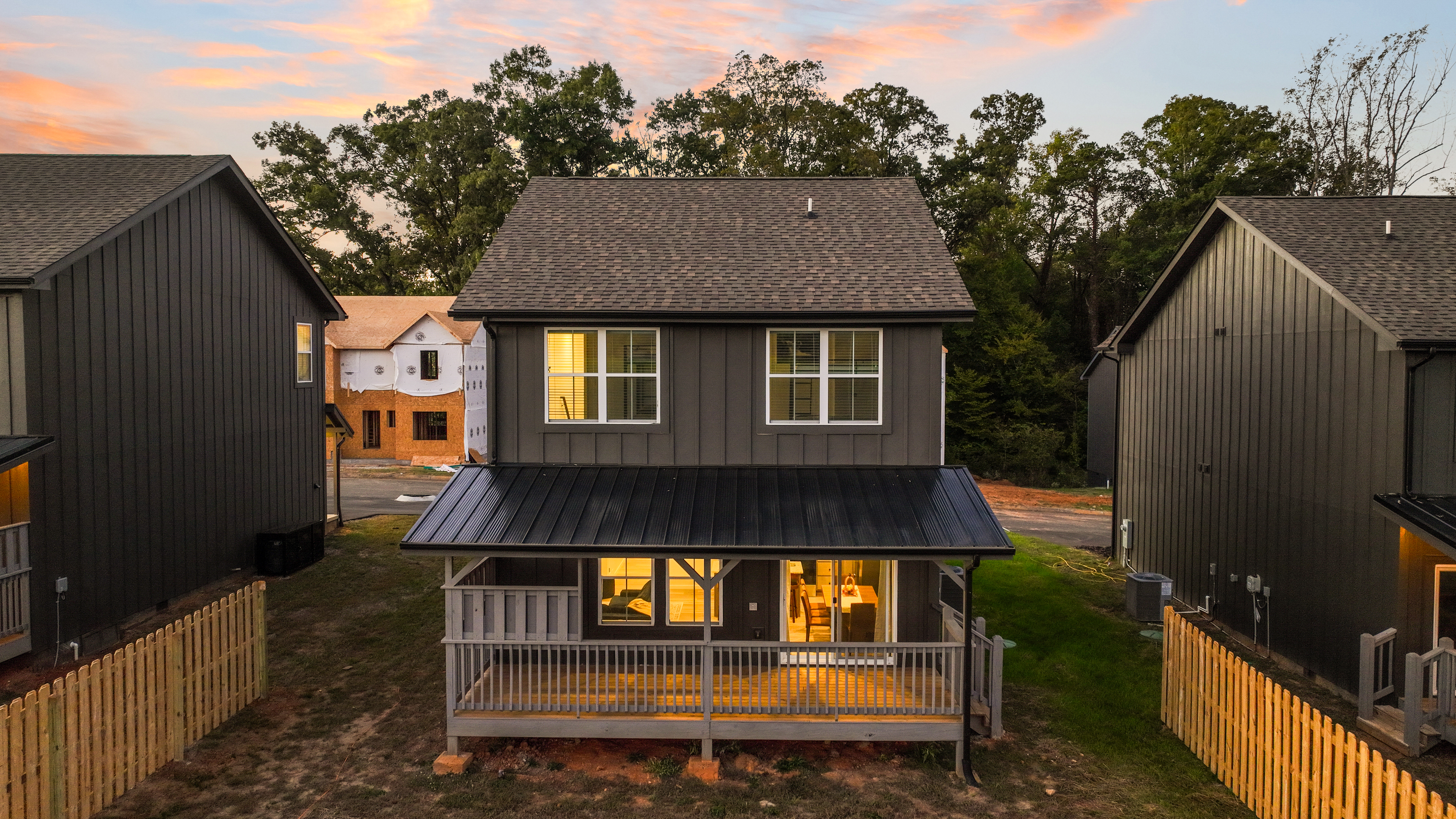 Charming dusk exterior with covered porch, warm glow, and fenced yard