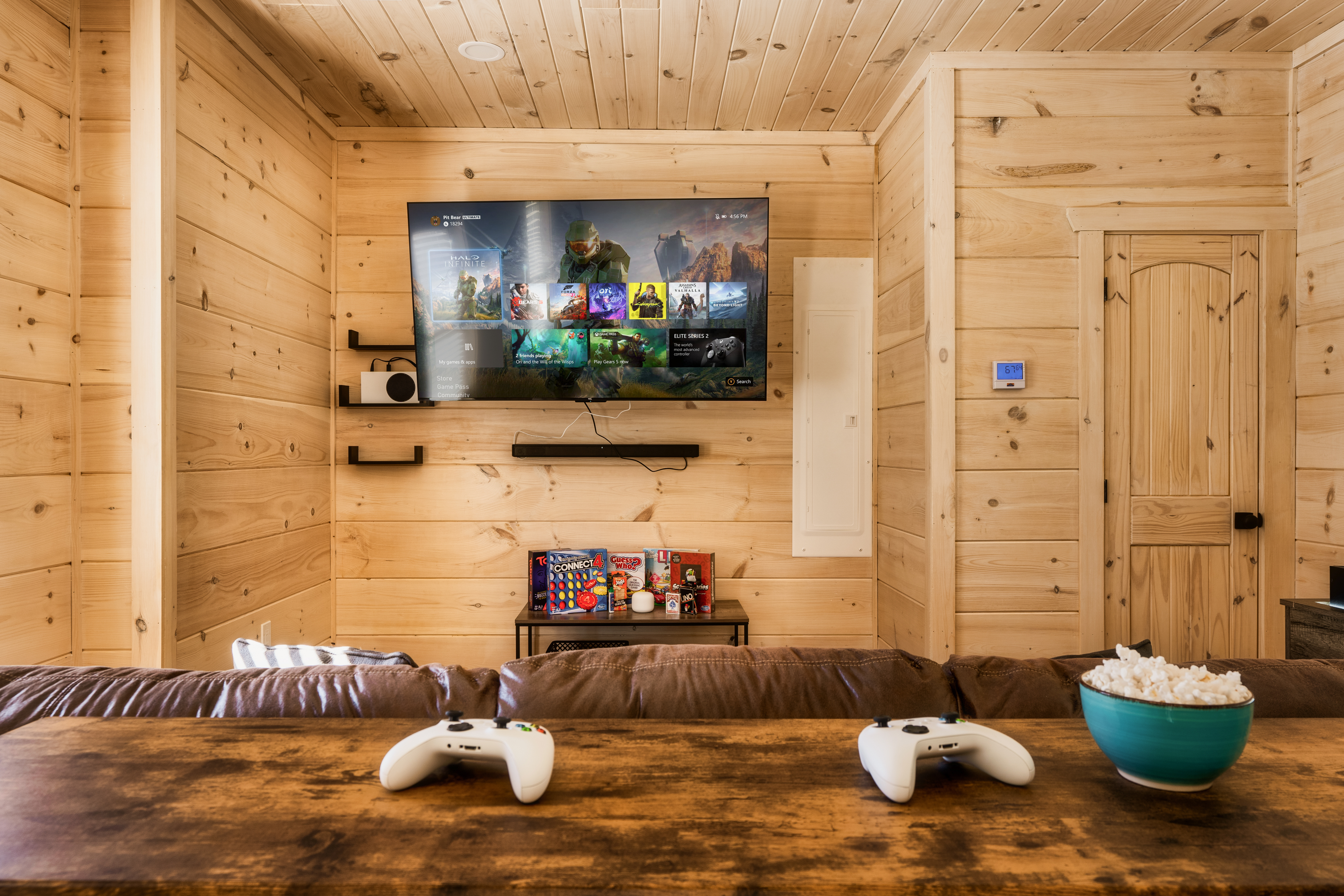 Cozy cabin game lounge with big-screen TV, Xbox setup, and snack-ready seating
