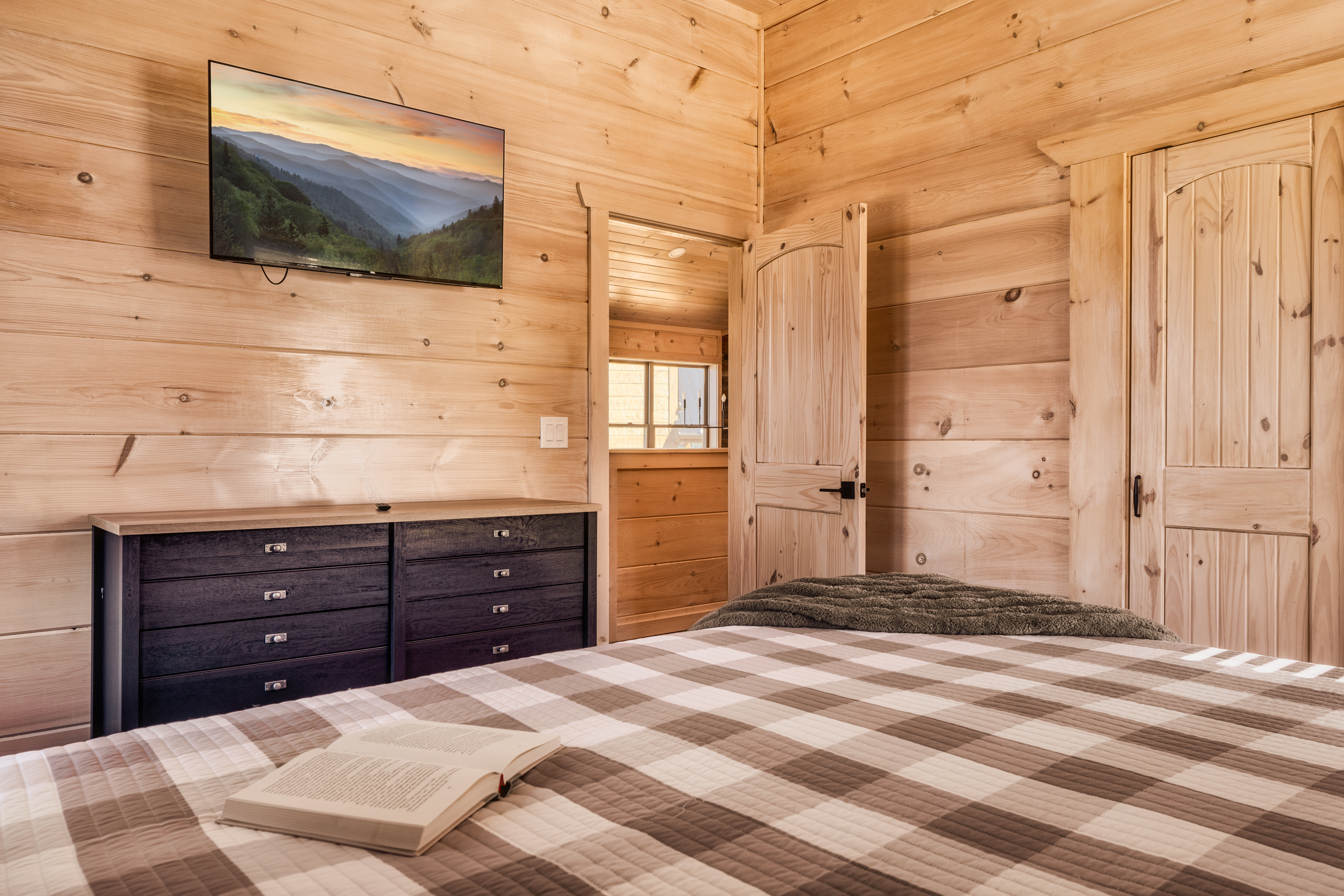 Cozy wood-lined cabin bedroom with plaid bedding and TV