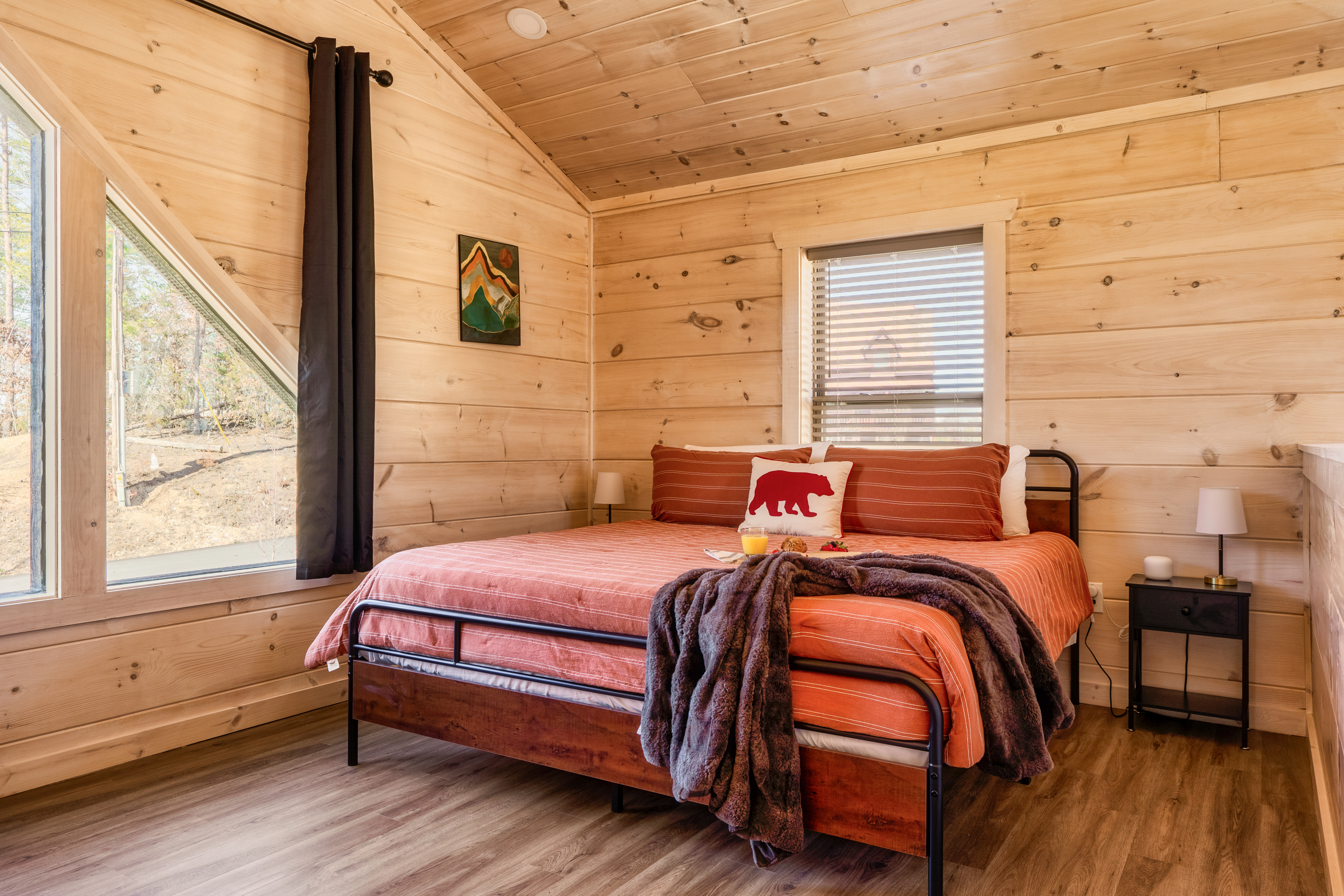 Cozy wood-lined bedroom with large windows and peaceful woodland views