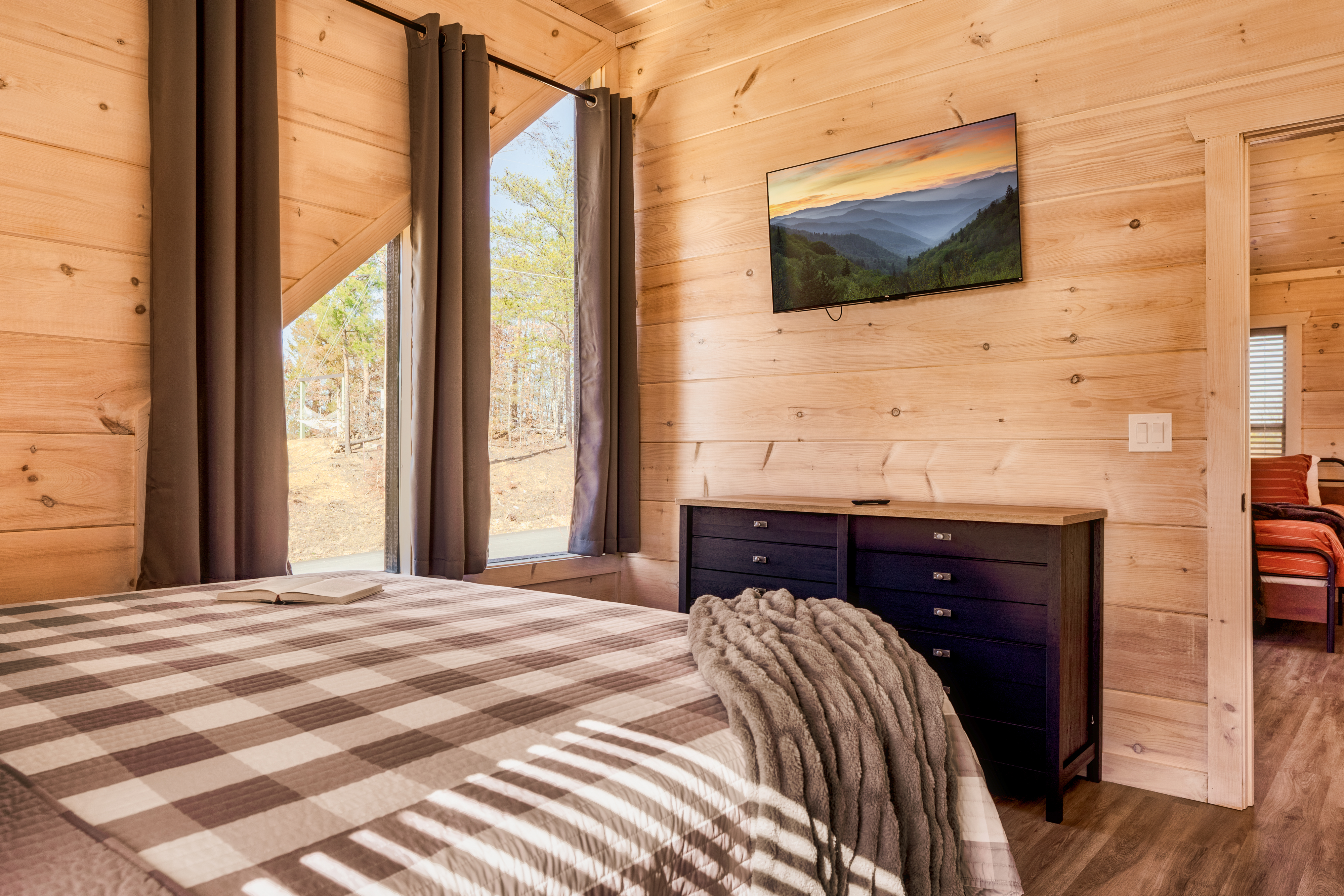 Cozy cabin bedroom with forest views, TV, and warm wood interiors