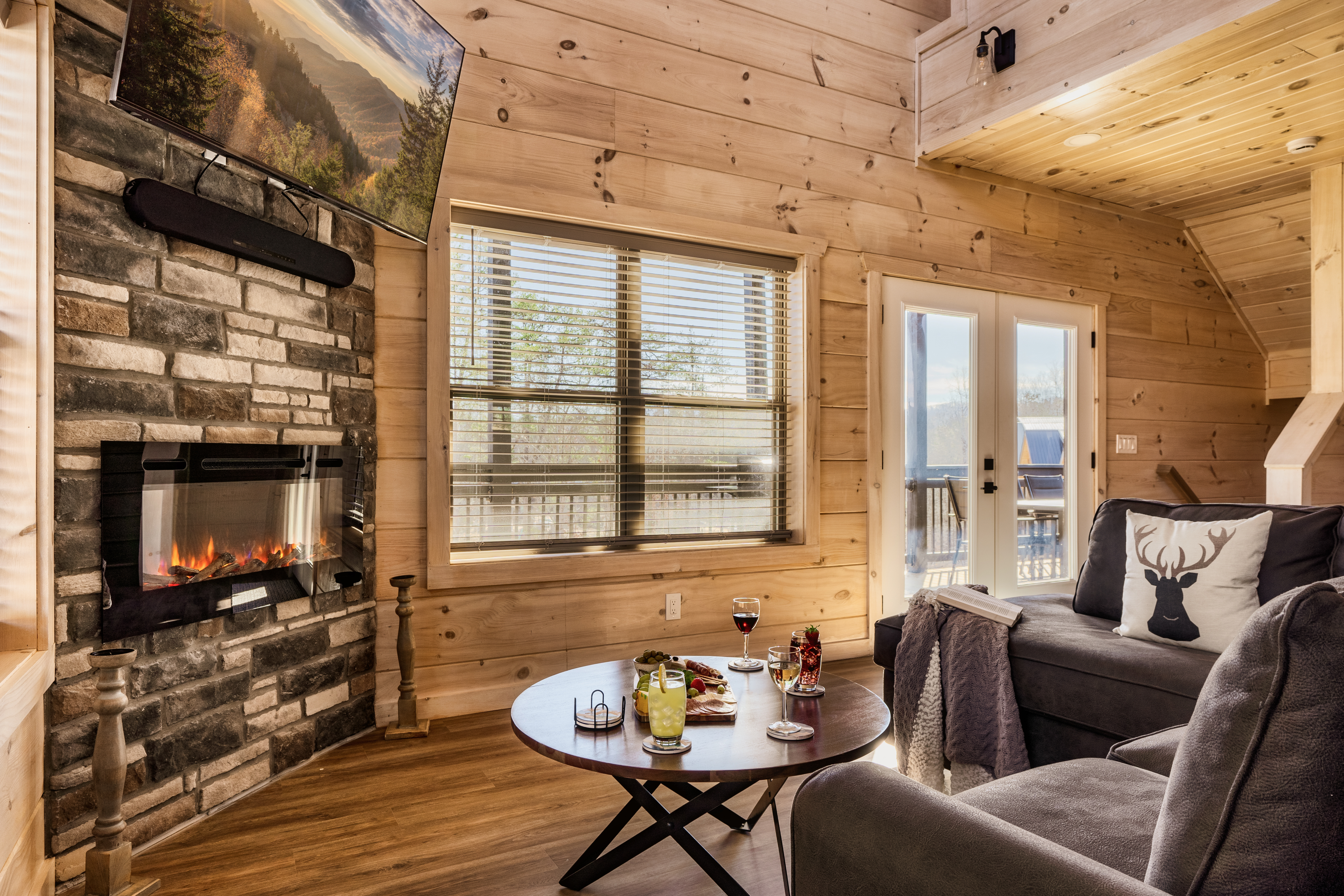 Cozy cabin living room with stone fireplace, deck access, and warm wood charm