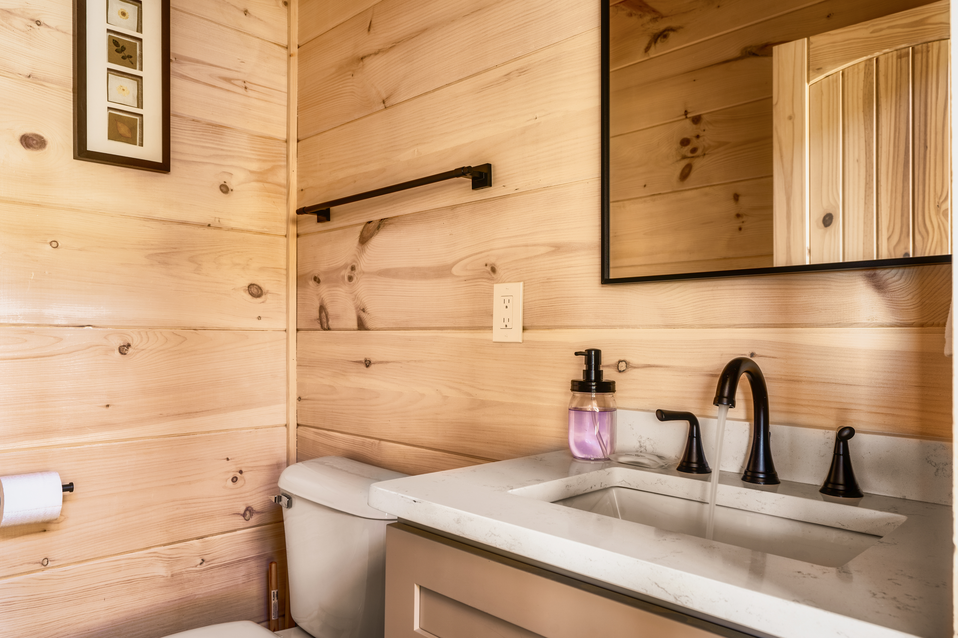 Cozy cabin-style bathroom with warm wood walls and modern black fixtures