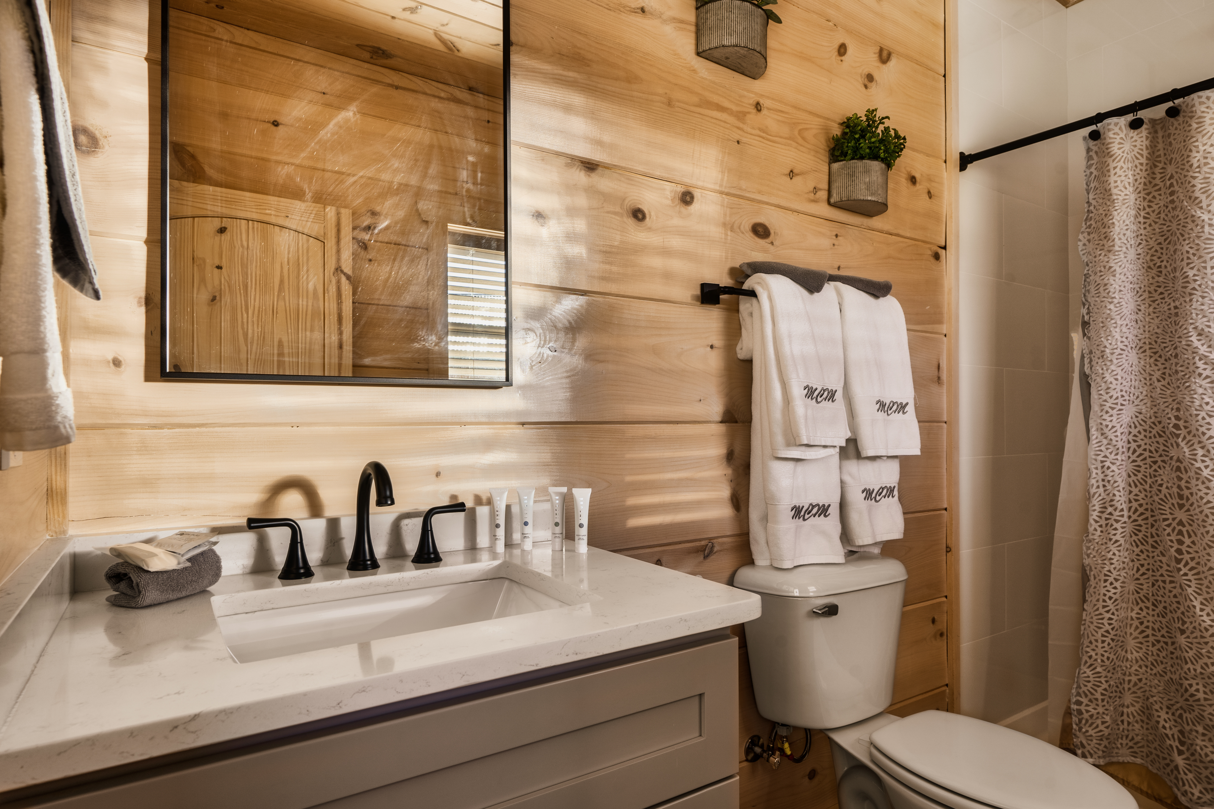 Rustic-modern bathroom with wood walls, luxe towels, and sleek black fixtures