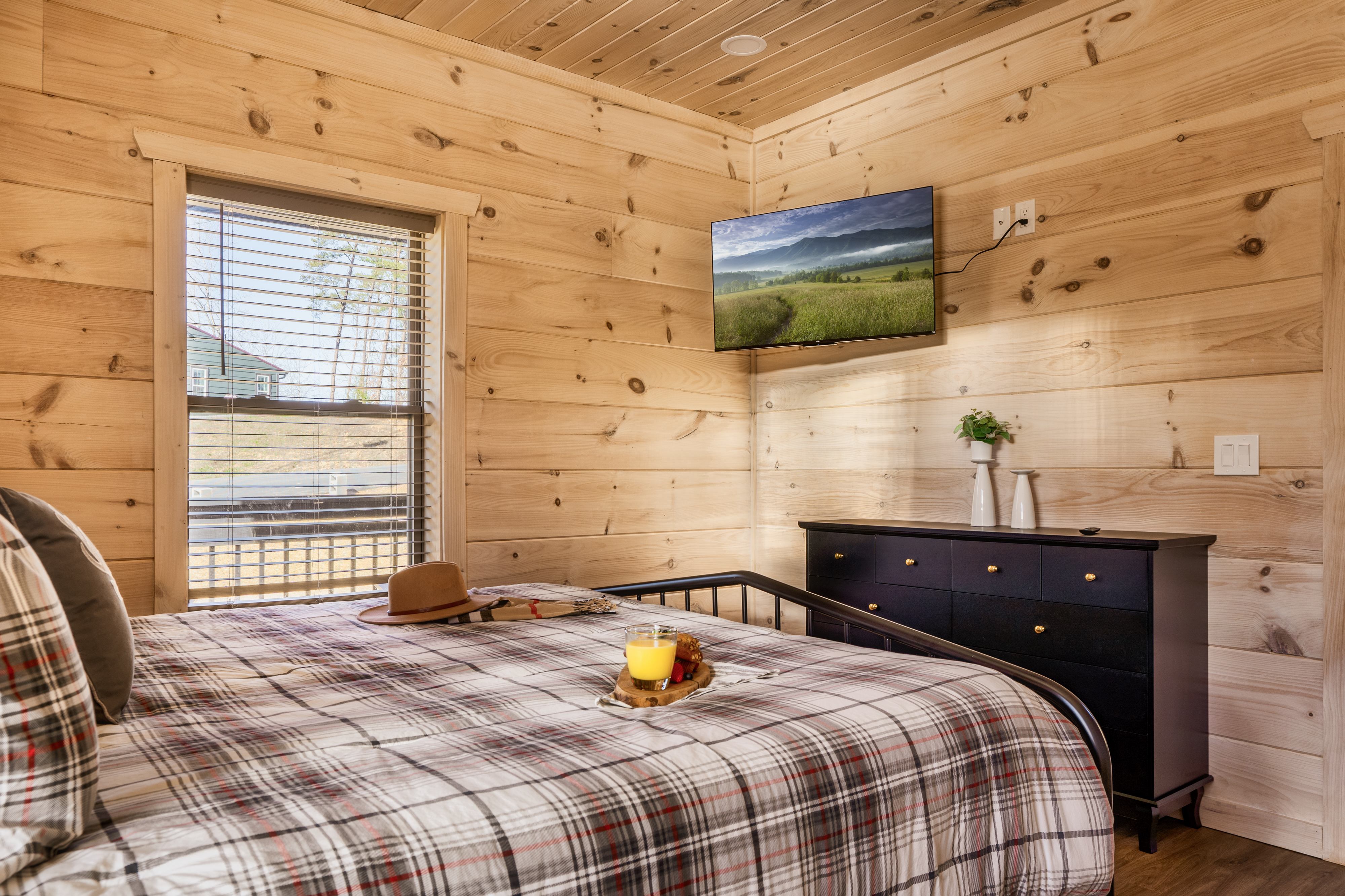 Cozy wood-lined bedroom with TV, natural light, and rustic cabin charm