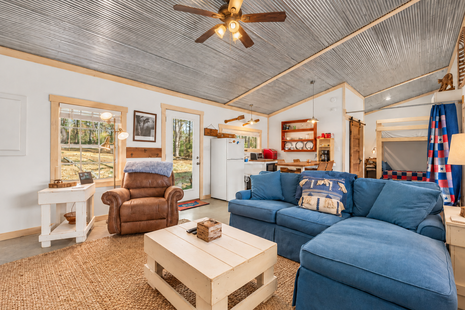 Living room with a double-size fold-out sleeper sofa for two guests; the connected open sleeping area has a triple bunk with three twin mattresses.