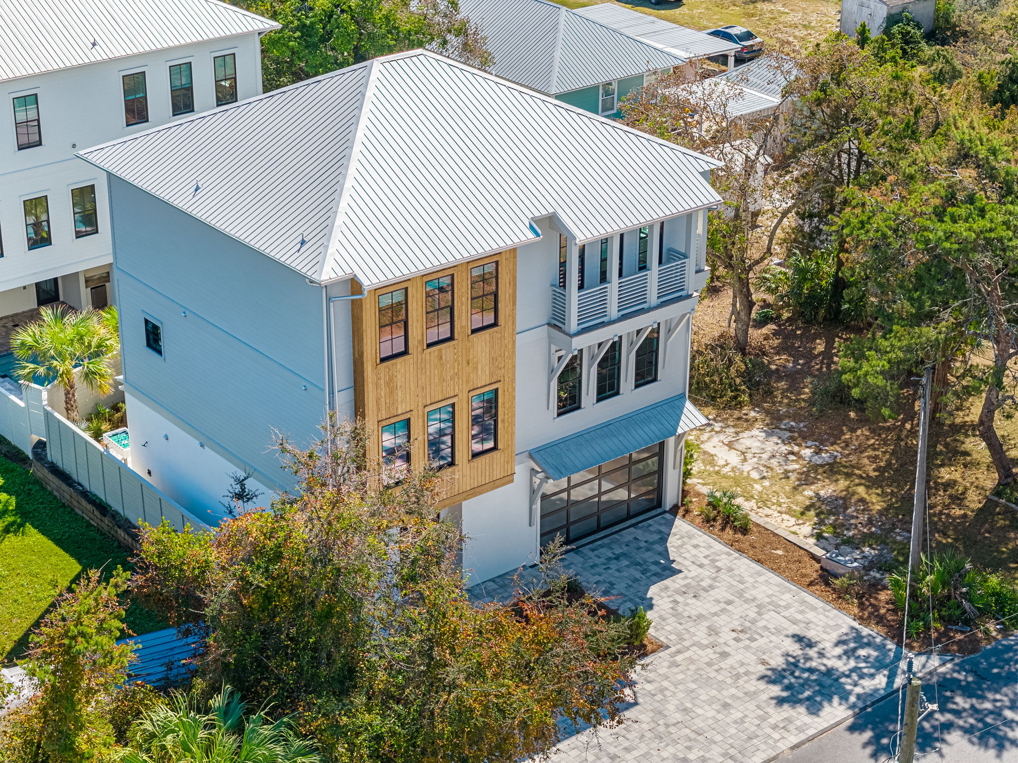 Modern coastal home with balcony, metal roof, and spacious driveway