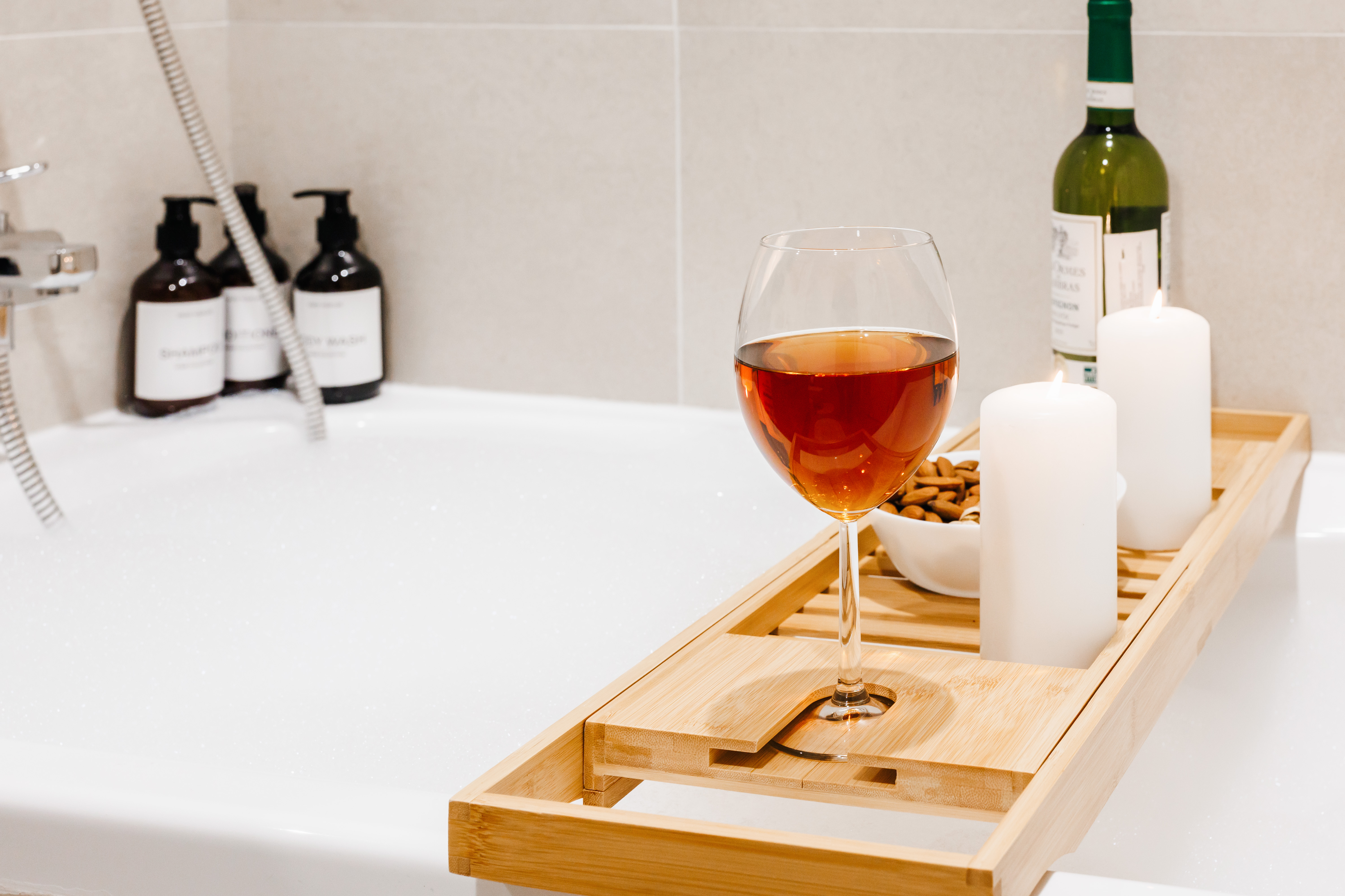 Spa-style soaking tub with bath tray, wine, candles, and luxe touches