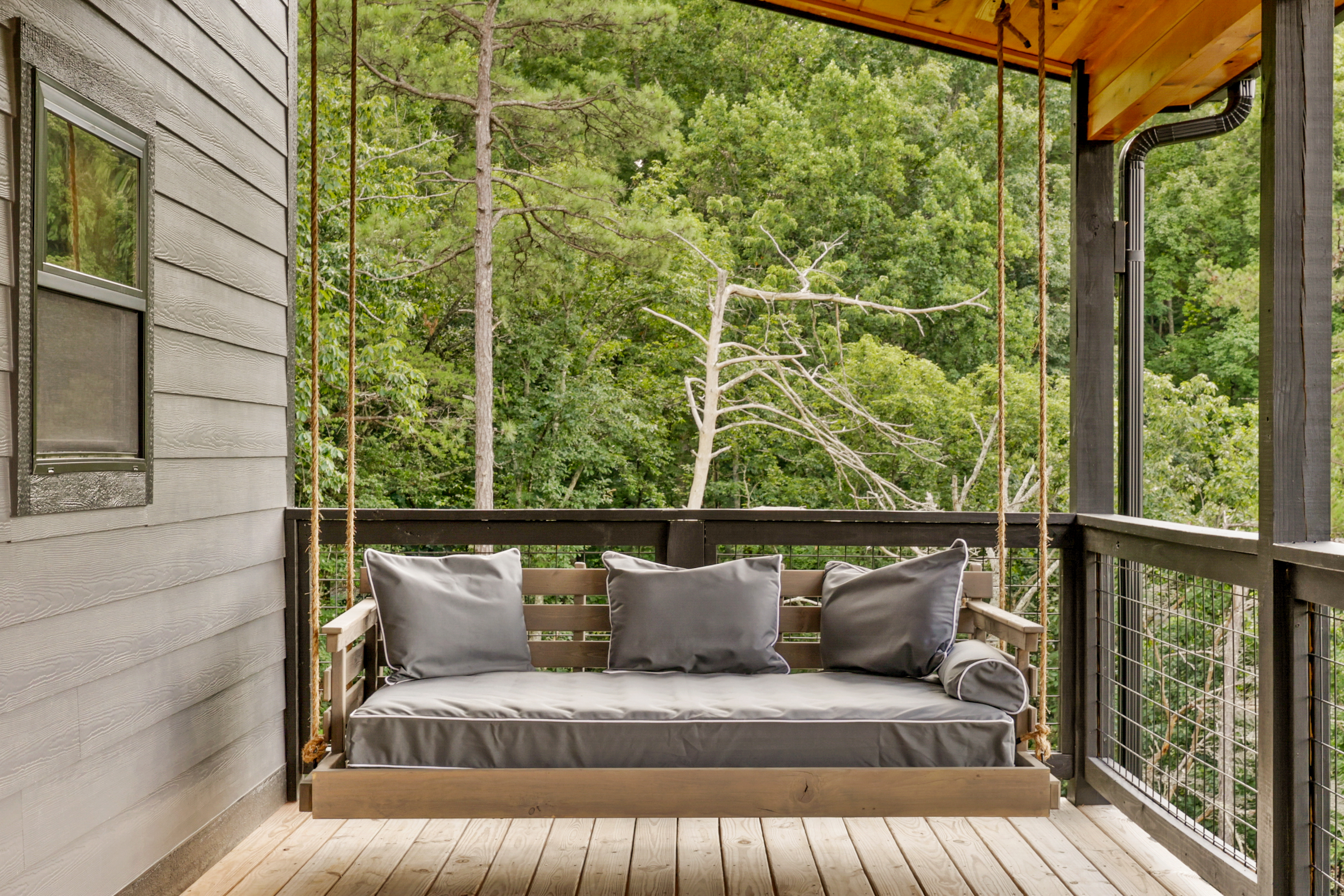 Covered porch swing bed with plush seating and serene forest views